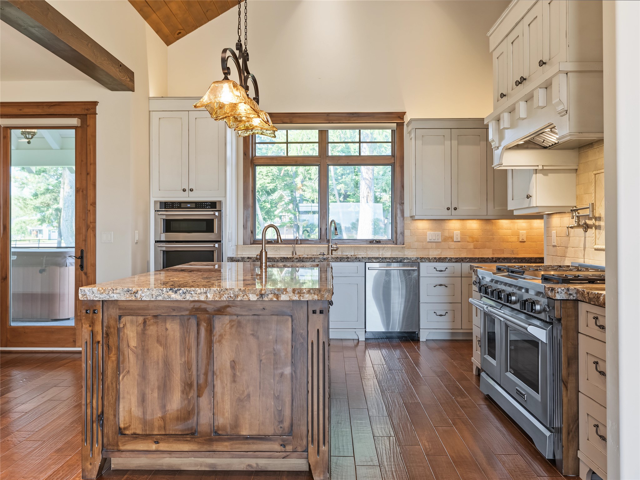 Kitchen with a rustic wood island, white cabinets, stainless-steel appliances, and a large sunlit window.