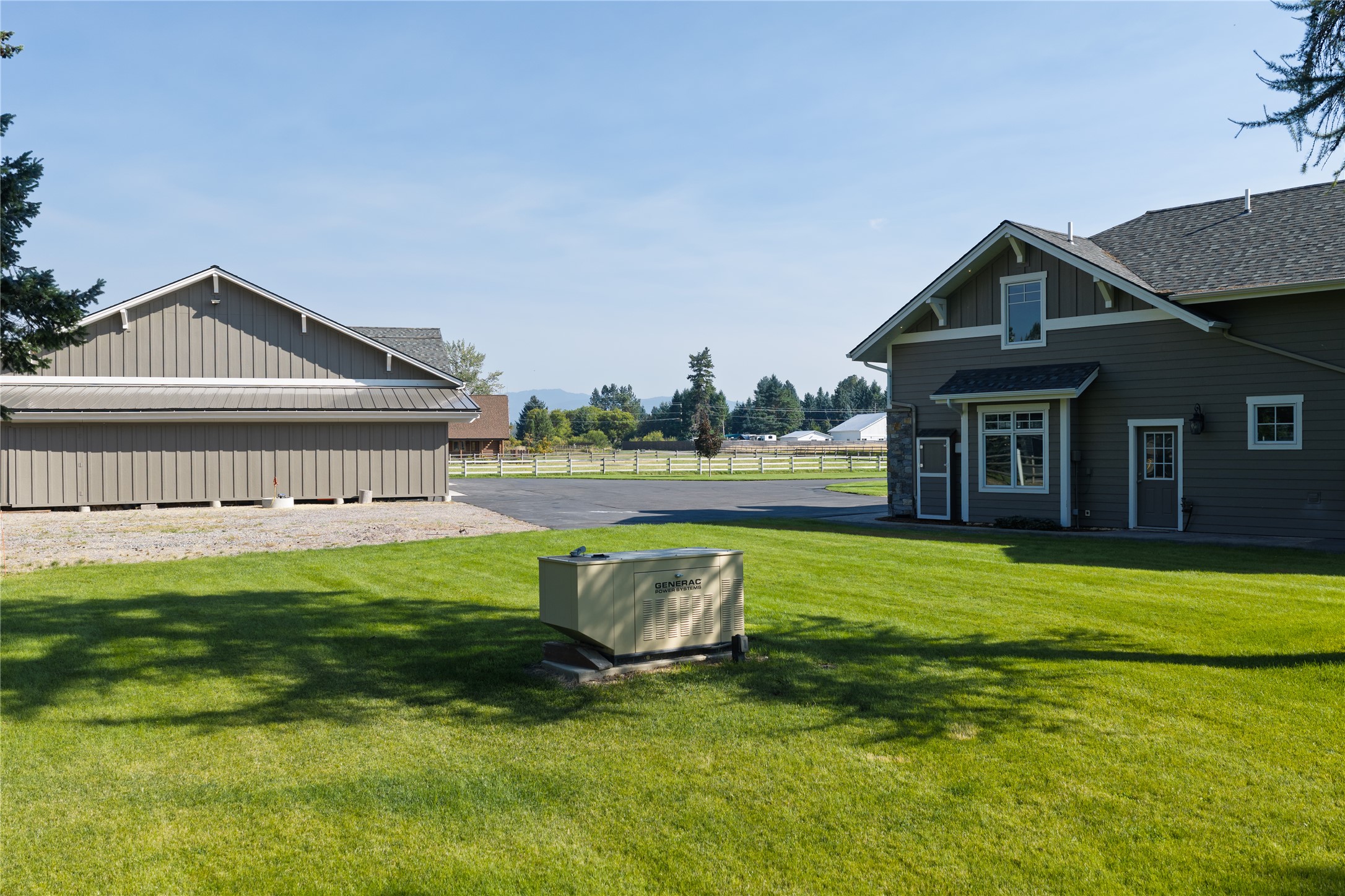 Home and outbuilding beside a green lawn, with a standby generator in the foreground.