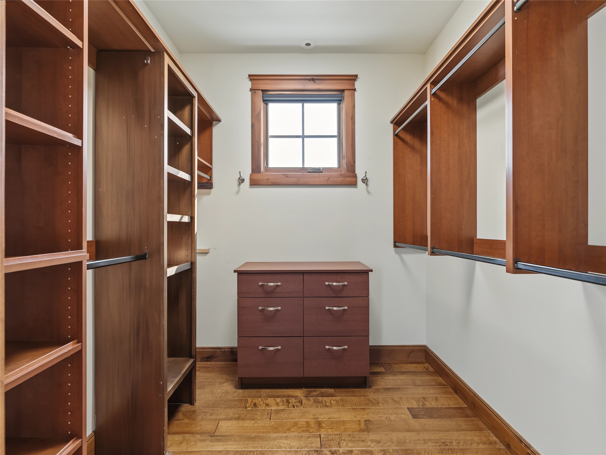 Walk-in closet with wood built-ins, hanging rods, a central drawer unit, and wood plank flooring.