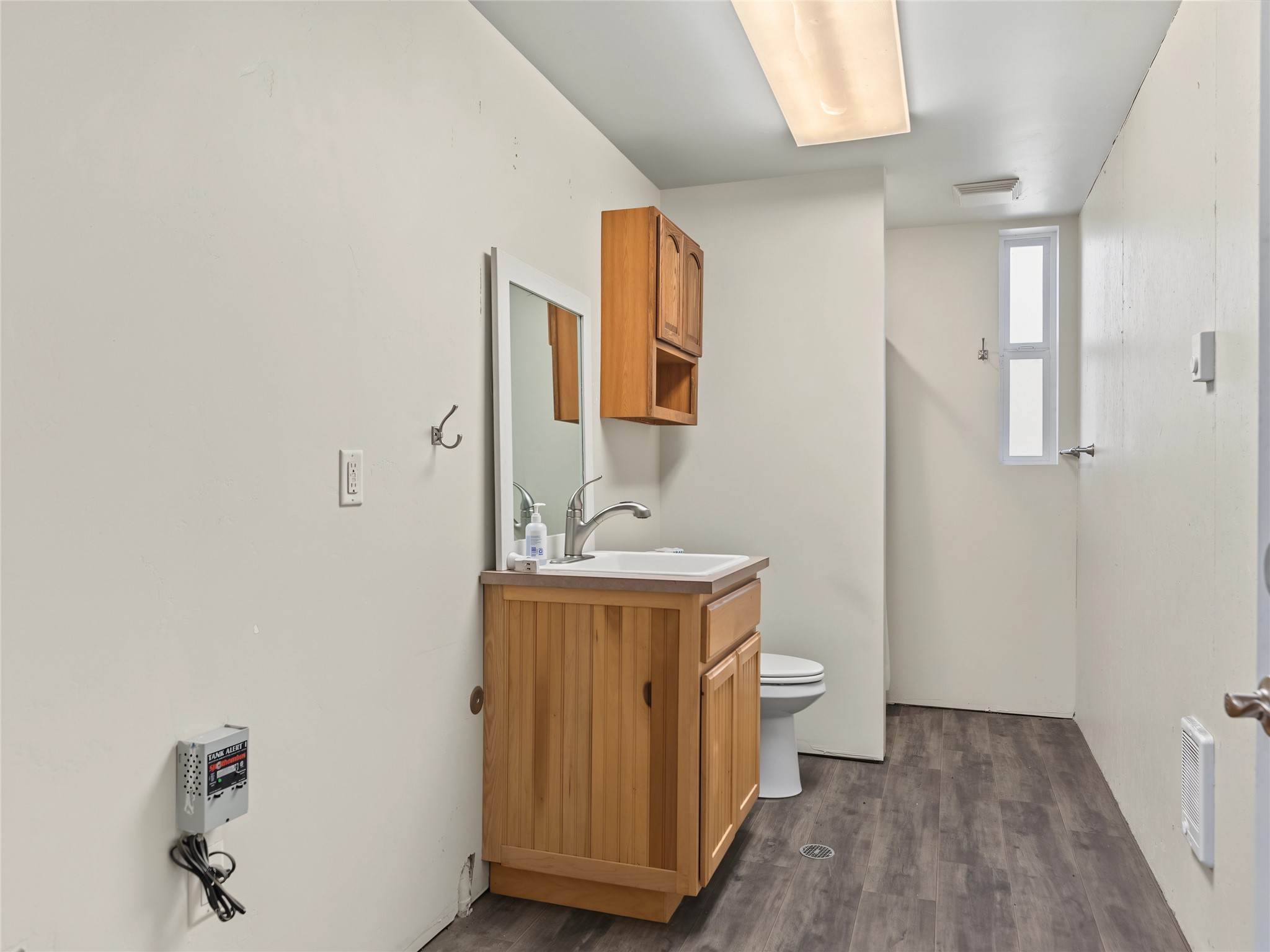 Bathroom with a wood vanity, white sink, toilet, and narrow frosted window.