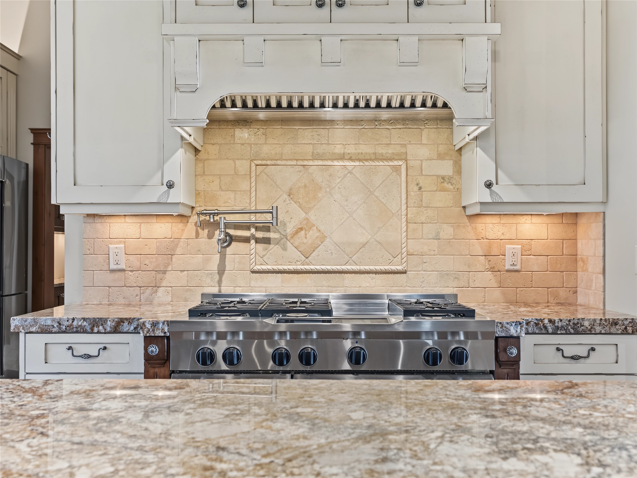 Kitchen with a stainless-steel gas range, stone tile backsplash, pot filler, and polished countertops.