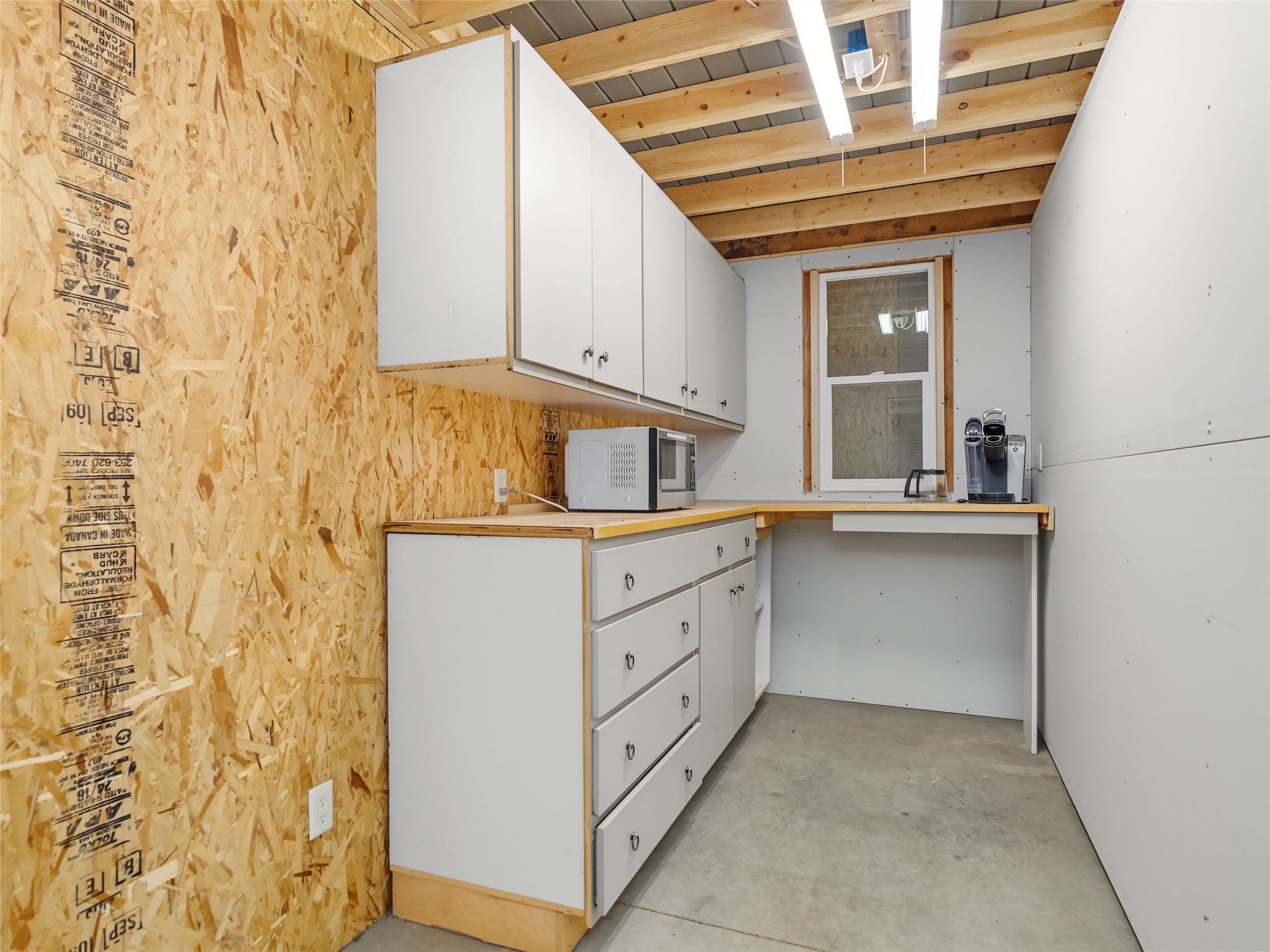 Utility kitchenette with white cabinets, a microwave, and an exposed OSB wall.