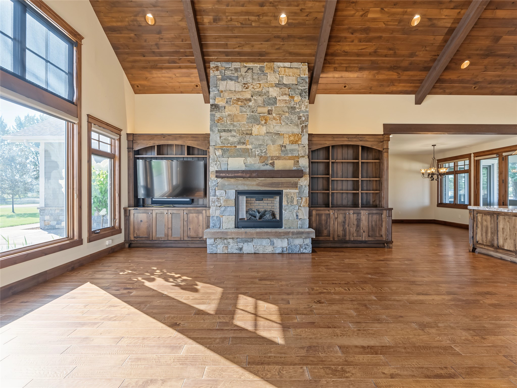 Vacant living room with a tall stone fireplace, built-in shelving, and a vaulted wood ceiling.