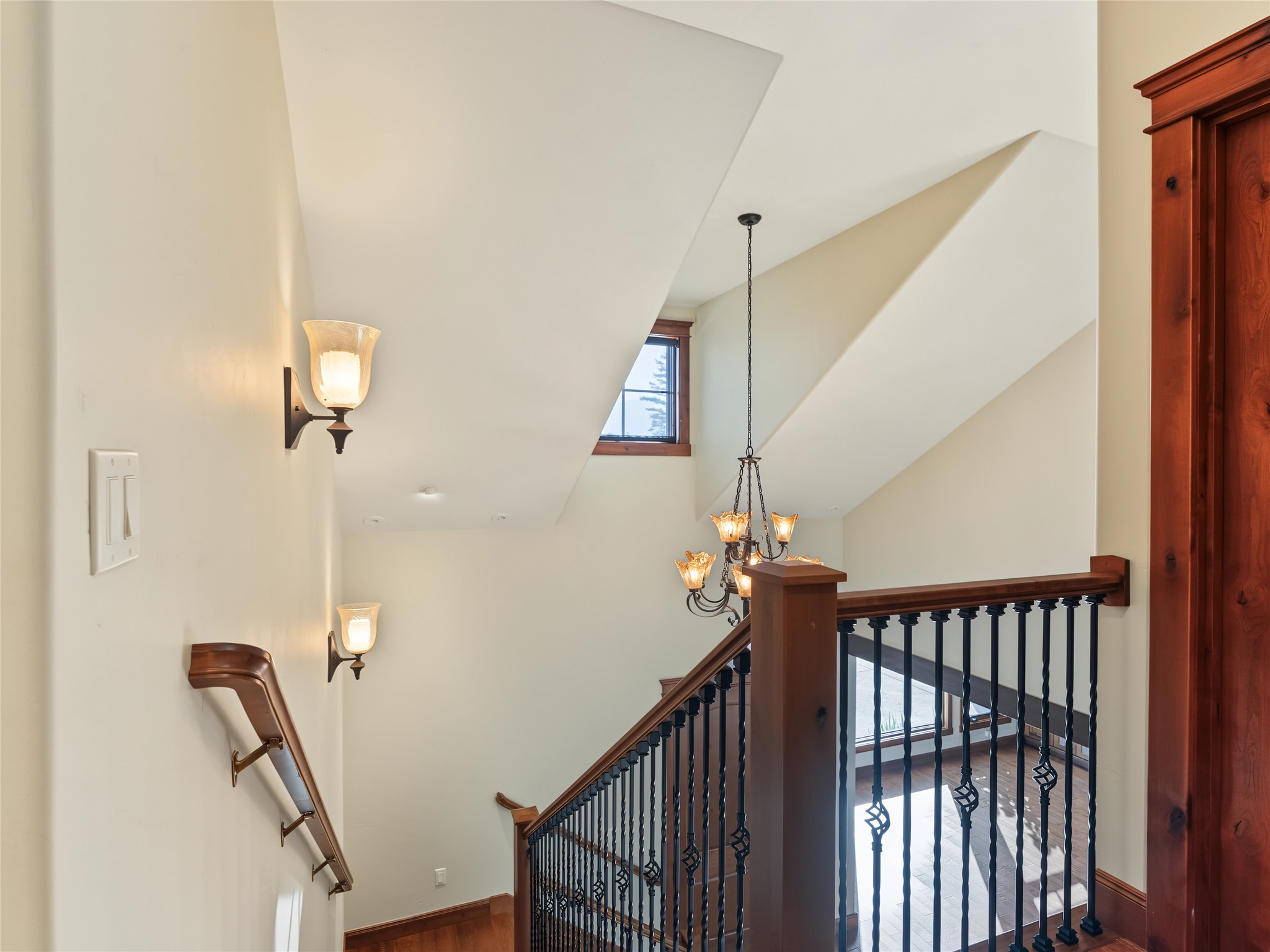 Staircase landing with dark wood railings, a chandelier, and a vaulted ceiling.