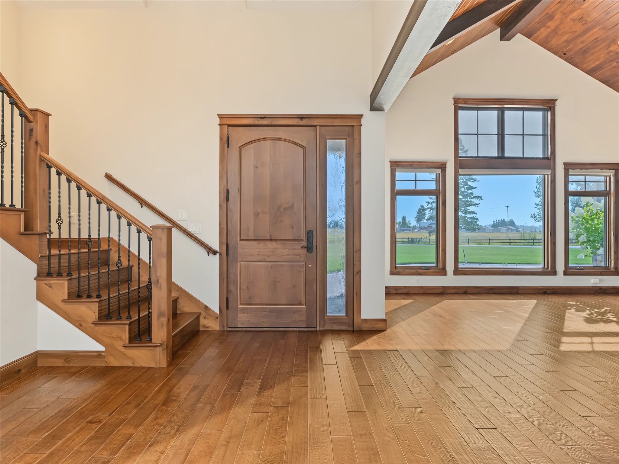 Vacant entryway with hardwood floors, a wood staircase, and large windows overlooking a lawn.
