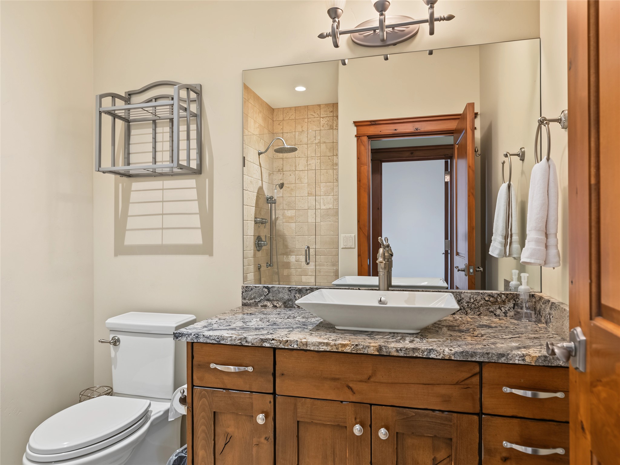 Bathroom with a wood vanity, granite countertop, vessel sink, and tiled shower.