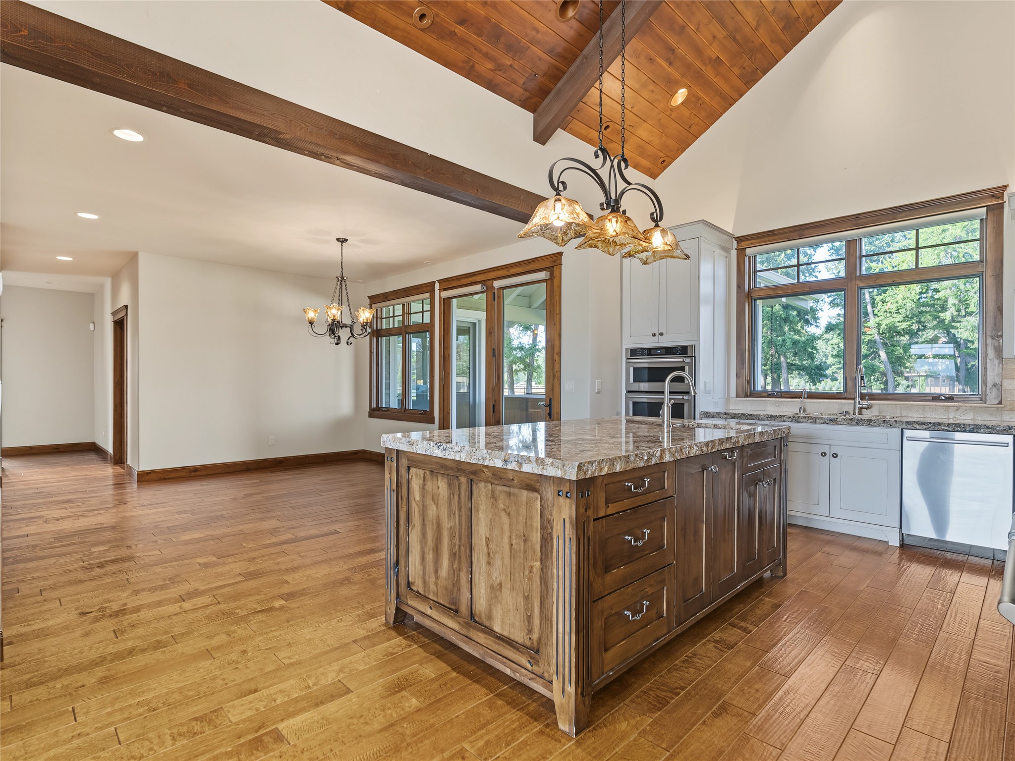 Vacant kitchen with a large wood island, stone countertop, vaulted wood ceiling, and broad windows.