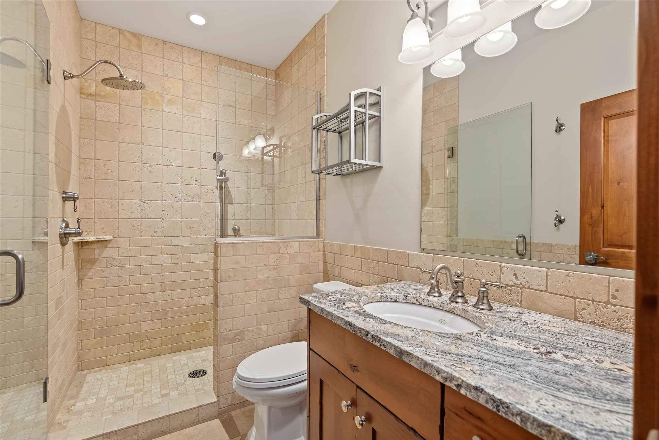 Bathroom with a glass-enclosed stone-tile shower and a wood vanity topped with granite.