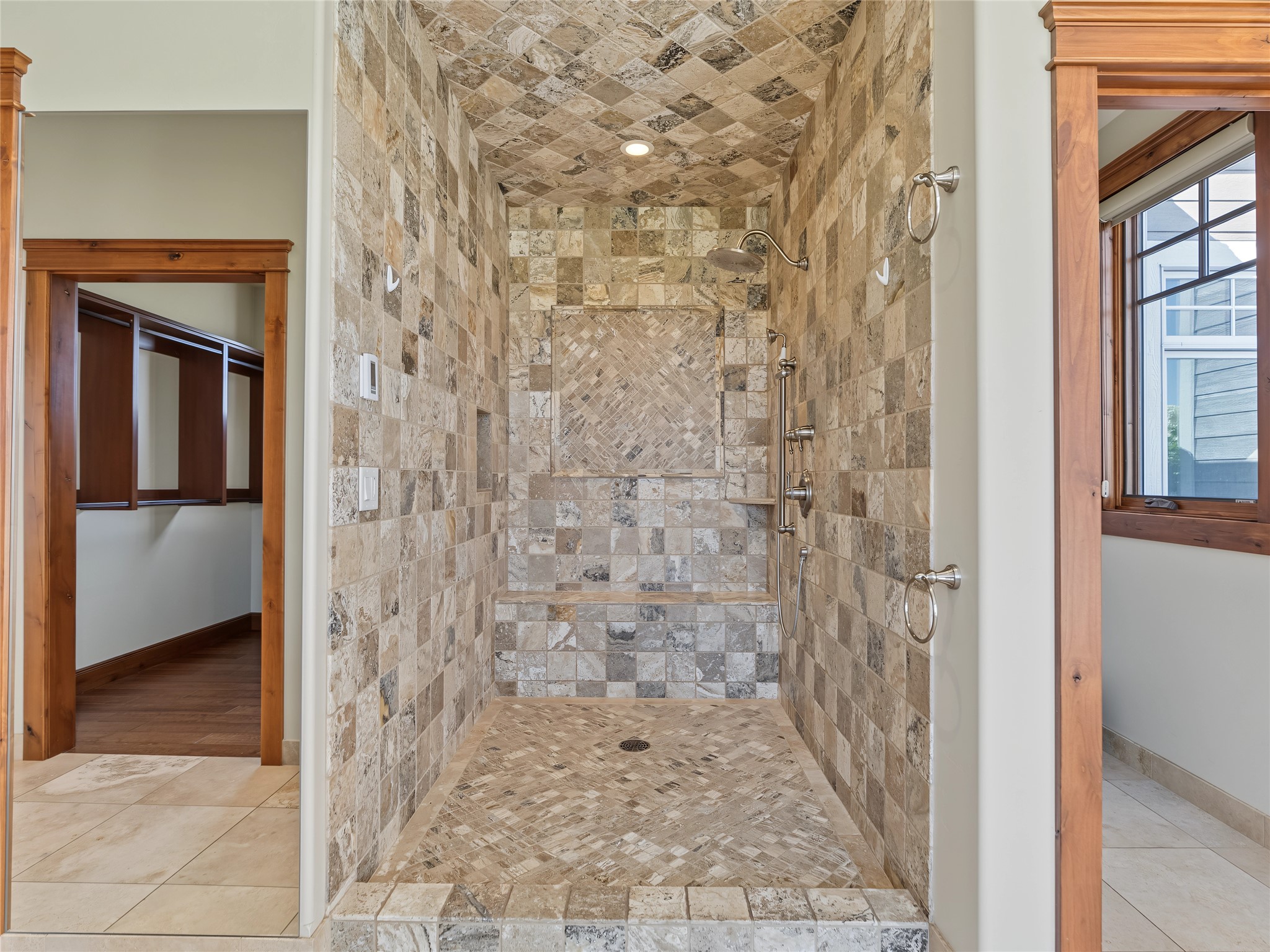 Walk-in stone-tiled shower with mosaic accent panel, built-in bench, and multiple fixtures.