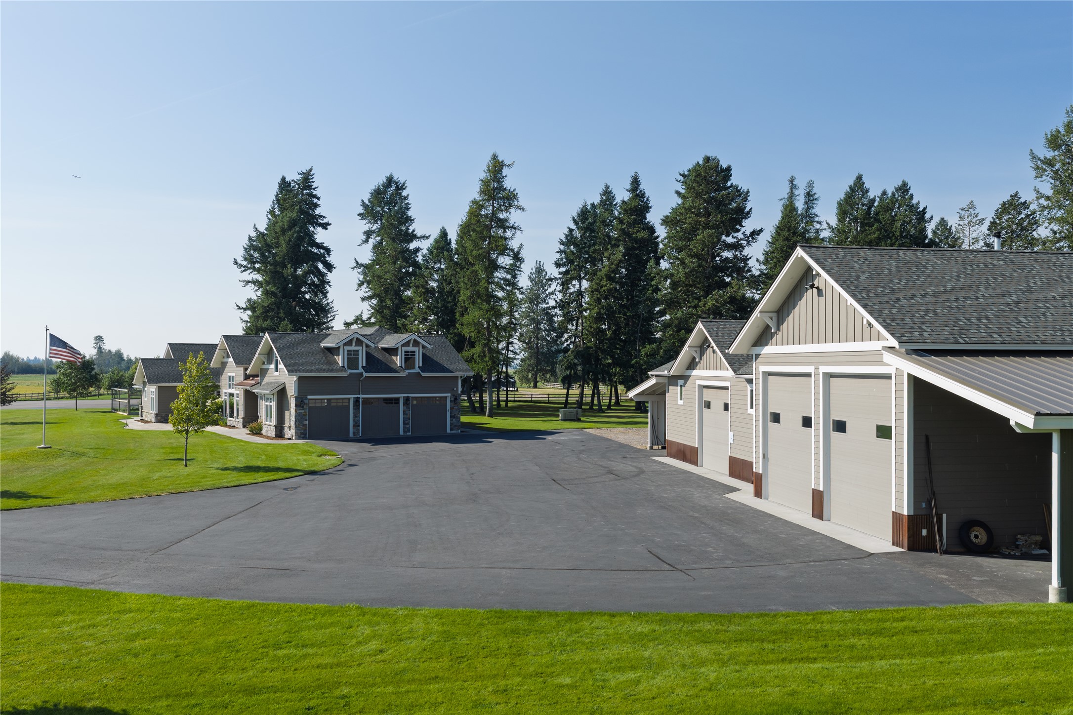 Multiple gray buildings with garage bays beside a broad paved driveway and green lawn.