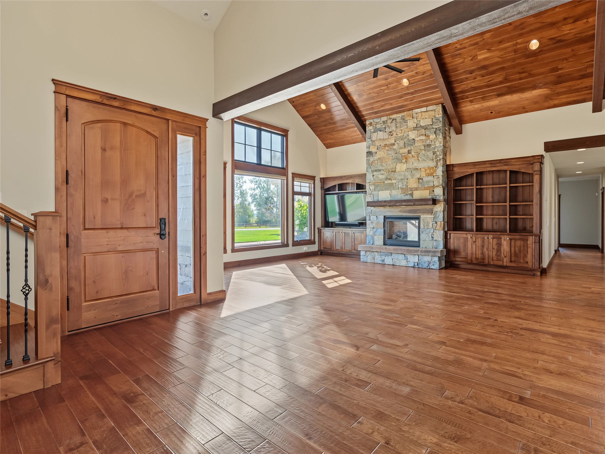 Living room with a vaulted wood ceiling, stone fireplace, built-in bookcases, and hardwood floors.