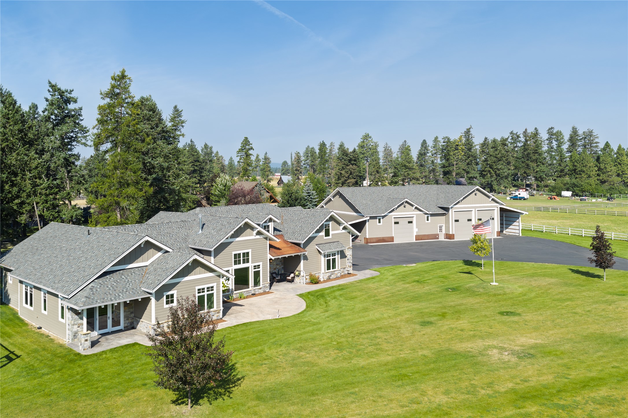 Aerial view of a gray home and large garage beside a broad lawn and paved parking area.