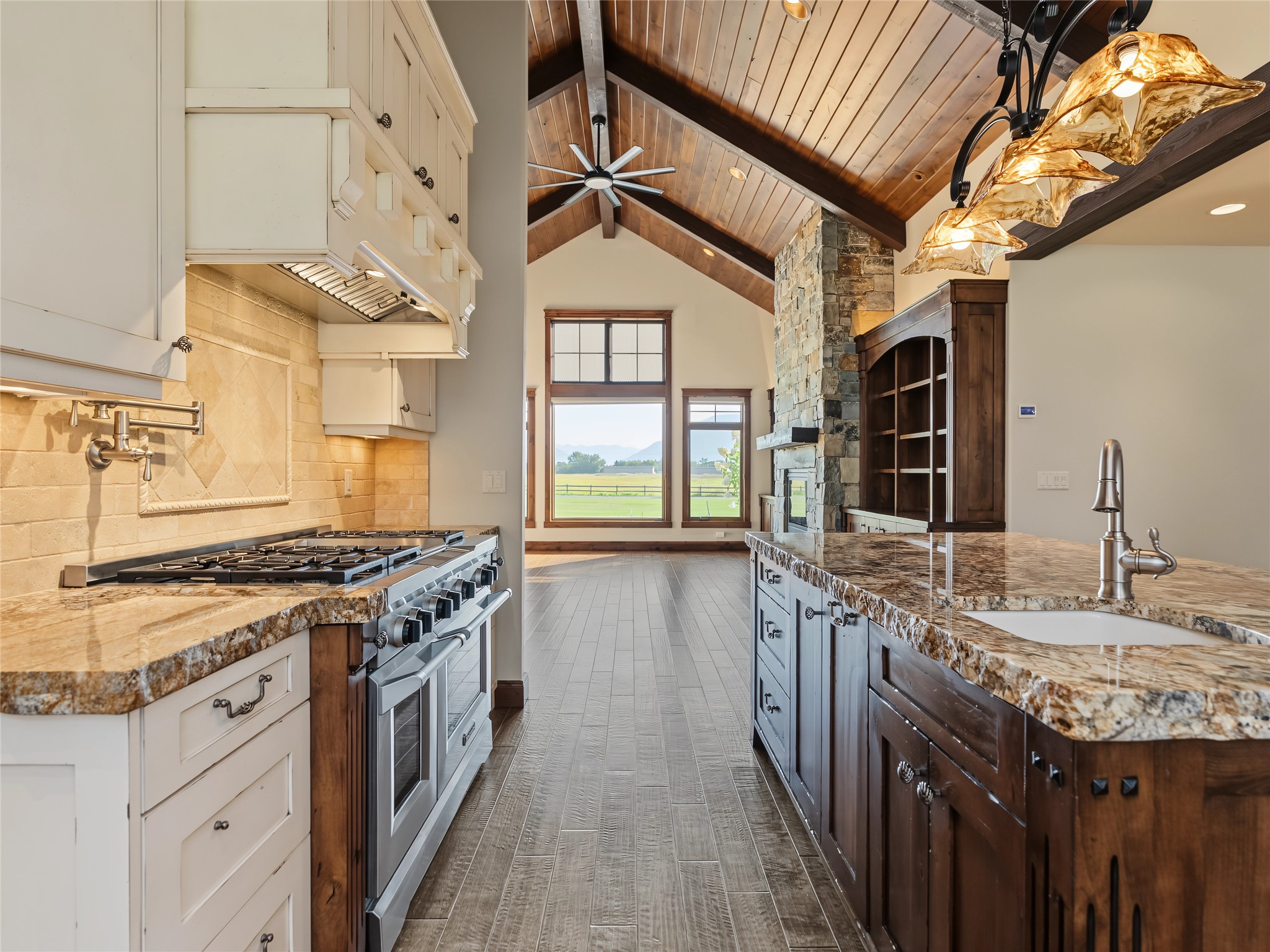 Kitchen with a professional gas range and large island, opening to a vaulted living area with a stone fireplace.