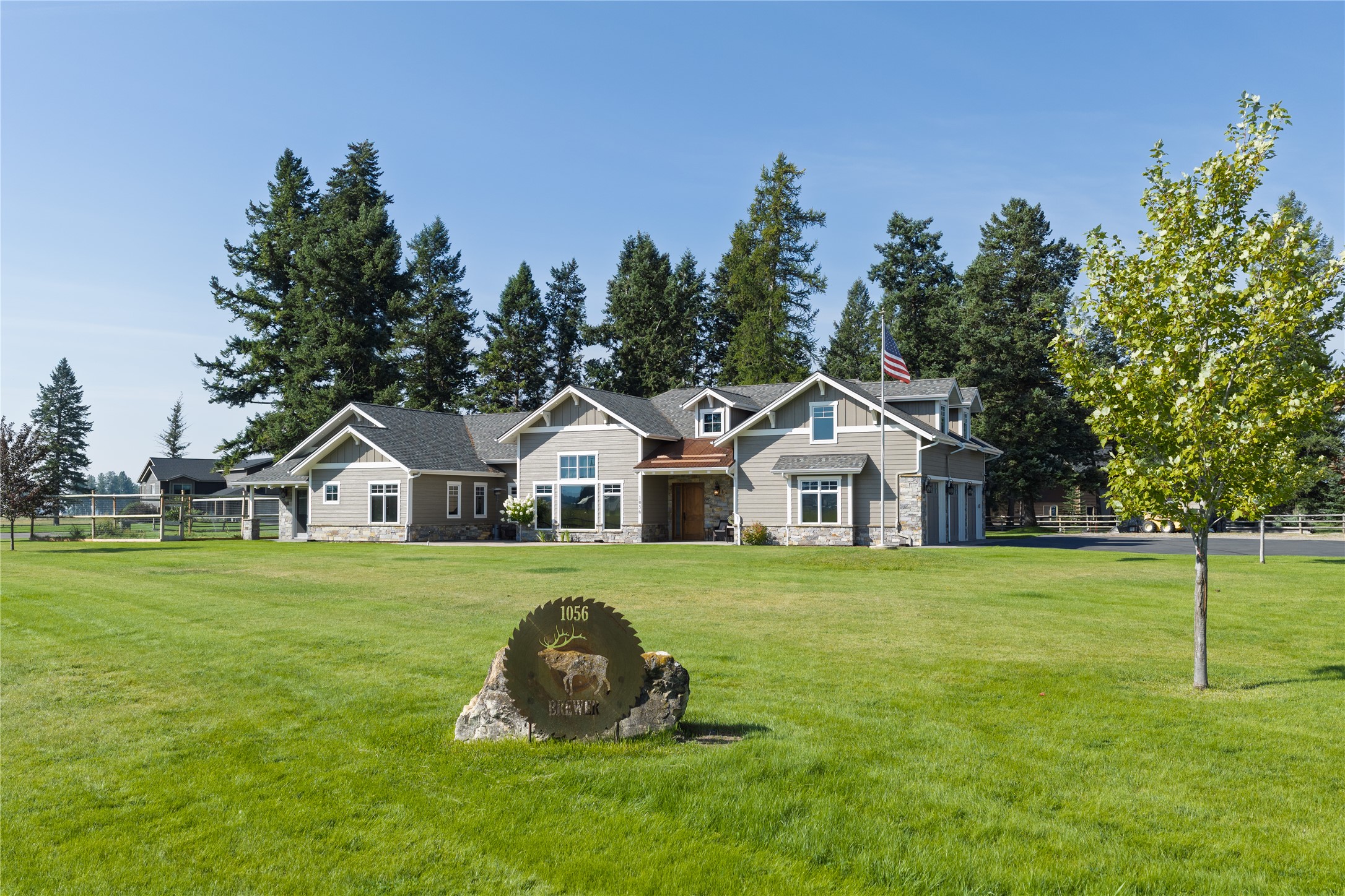 Gray-sided home with stone accents behind a broad lawn and a 1056 metal sign.