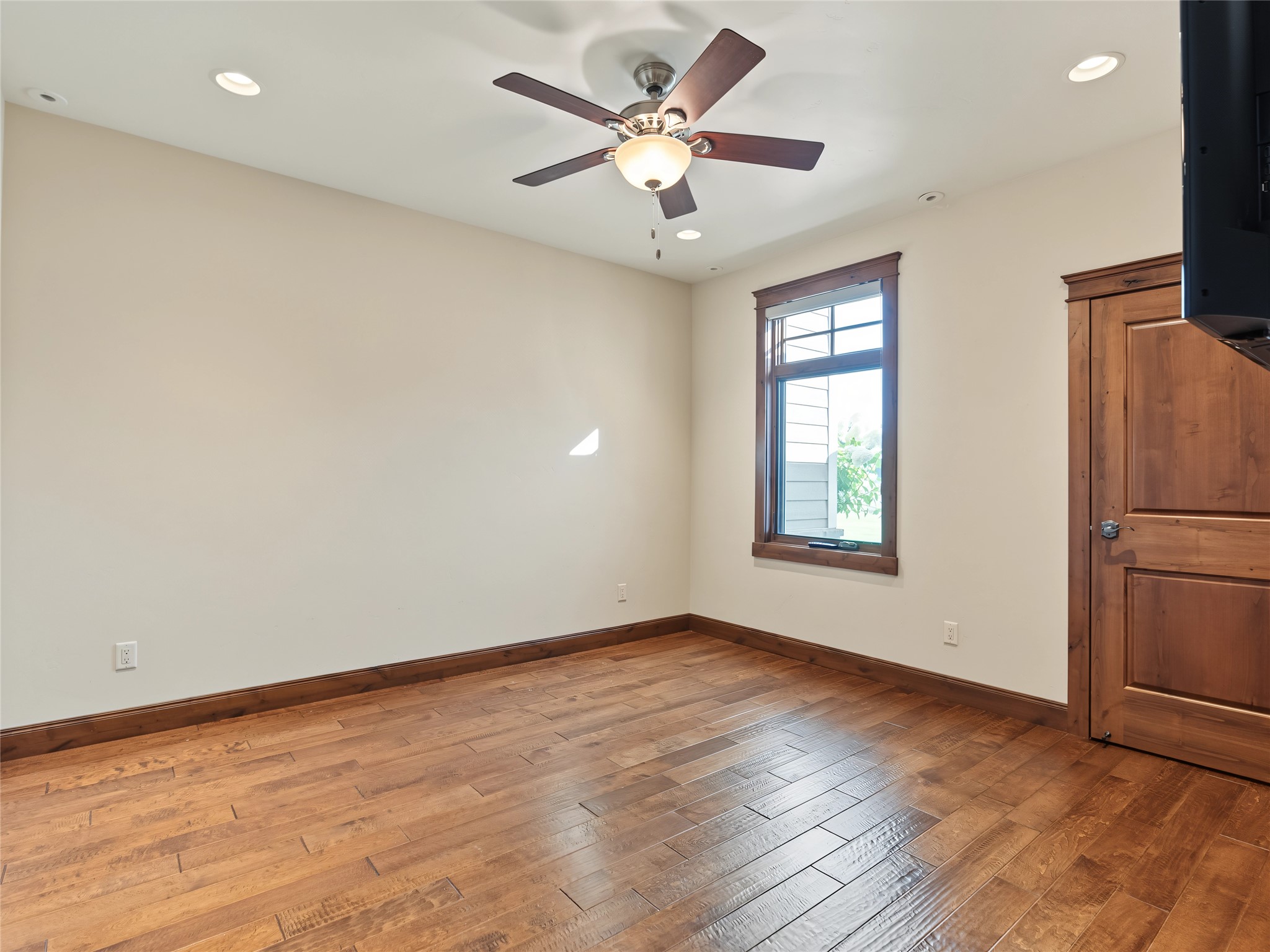 Empty kitchen with hardwood floors, a dark wood-trimmed window, and a ceiling fan.