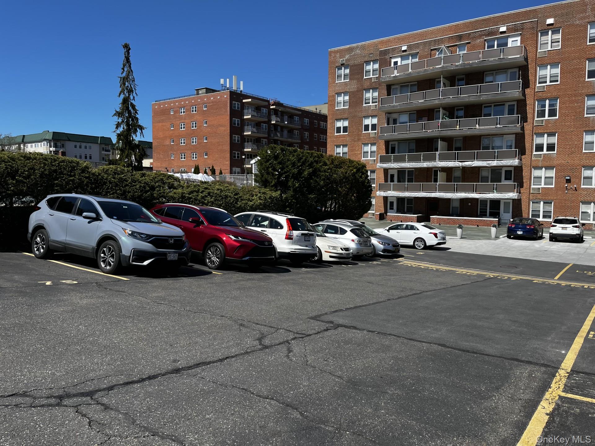 Brick apartment building with stacked balconies beside a parking lot filled with cars.
