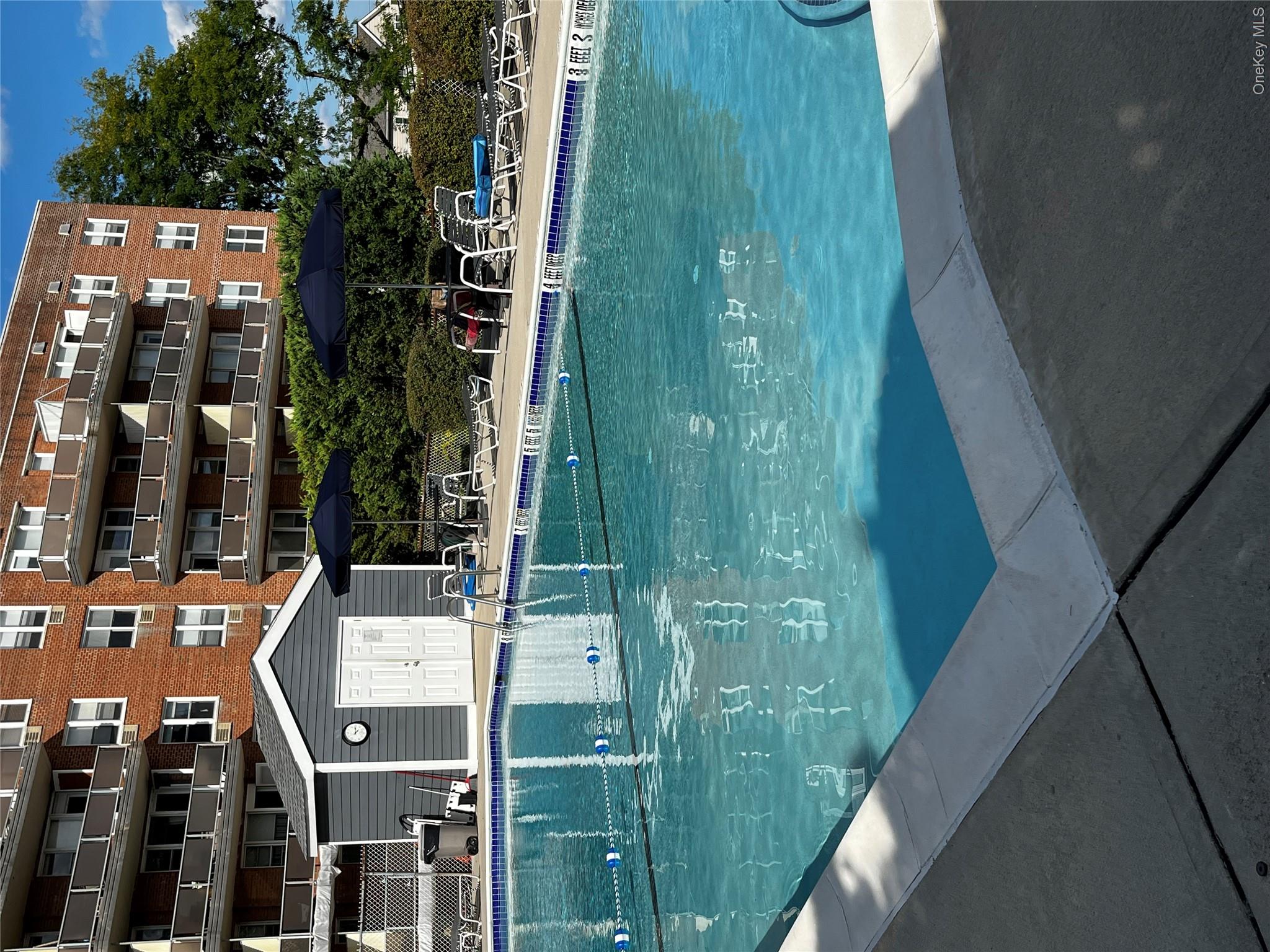 Outdoor swimming pool beside a brick apartment building, with lane markers and shaded lounge seating.