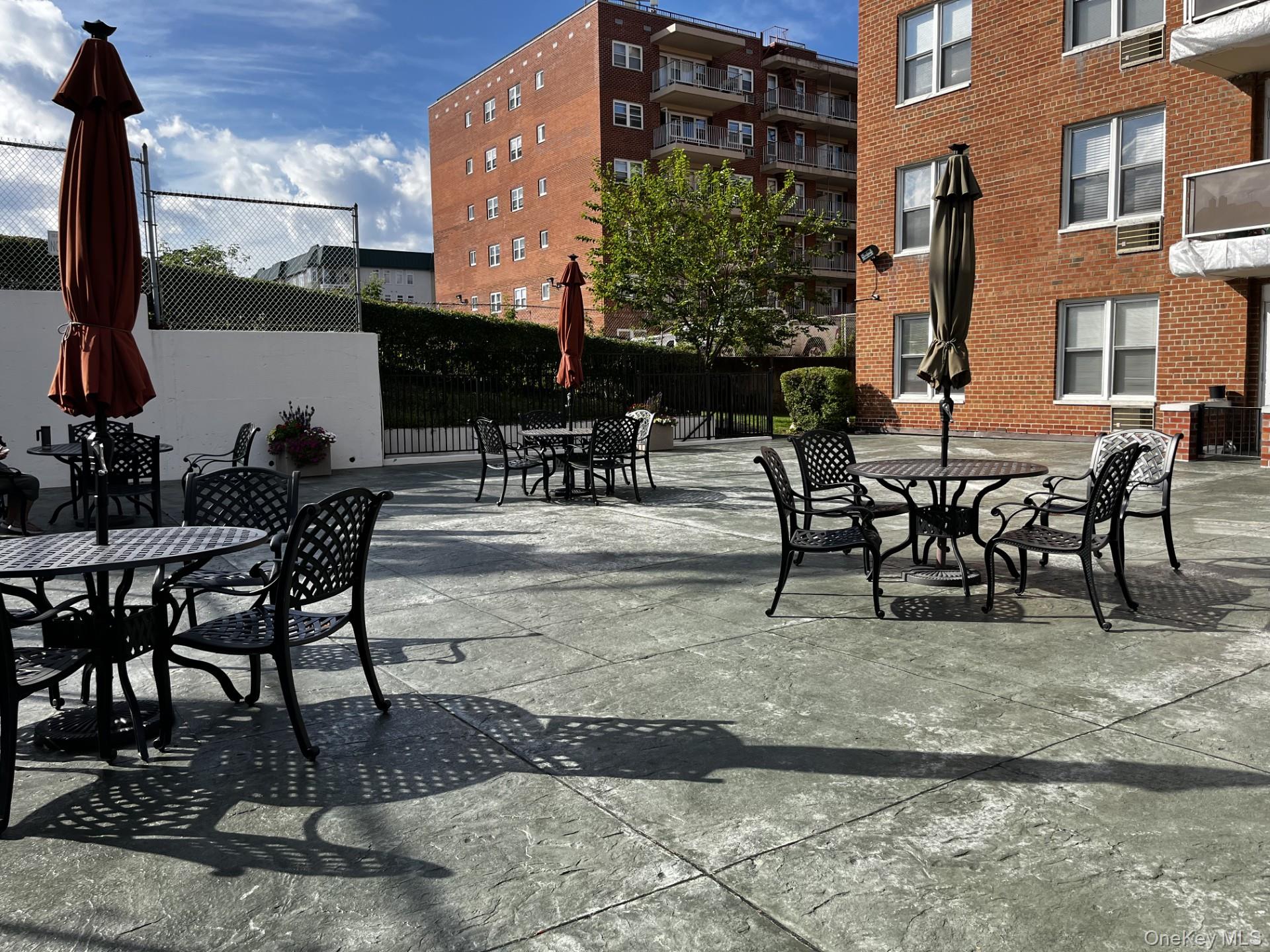 Apartment courtyard patio with black metal seating, closed umbrellas, and red-brick buildings.