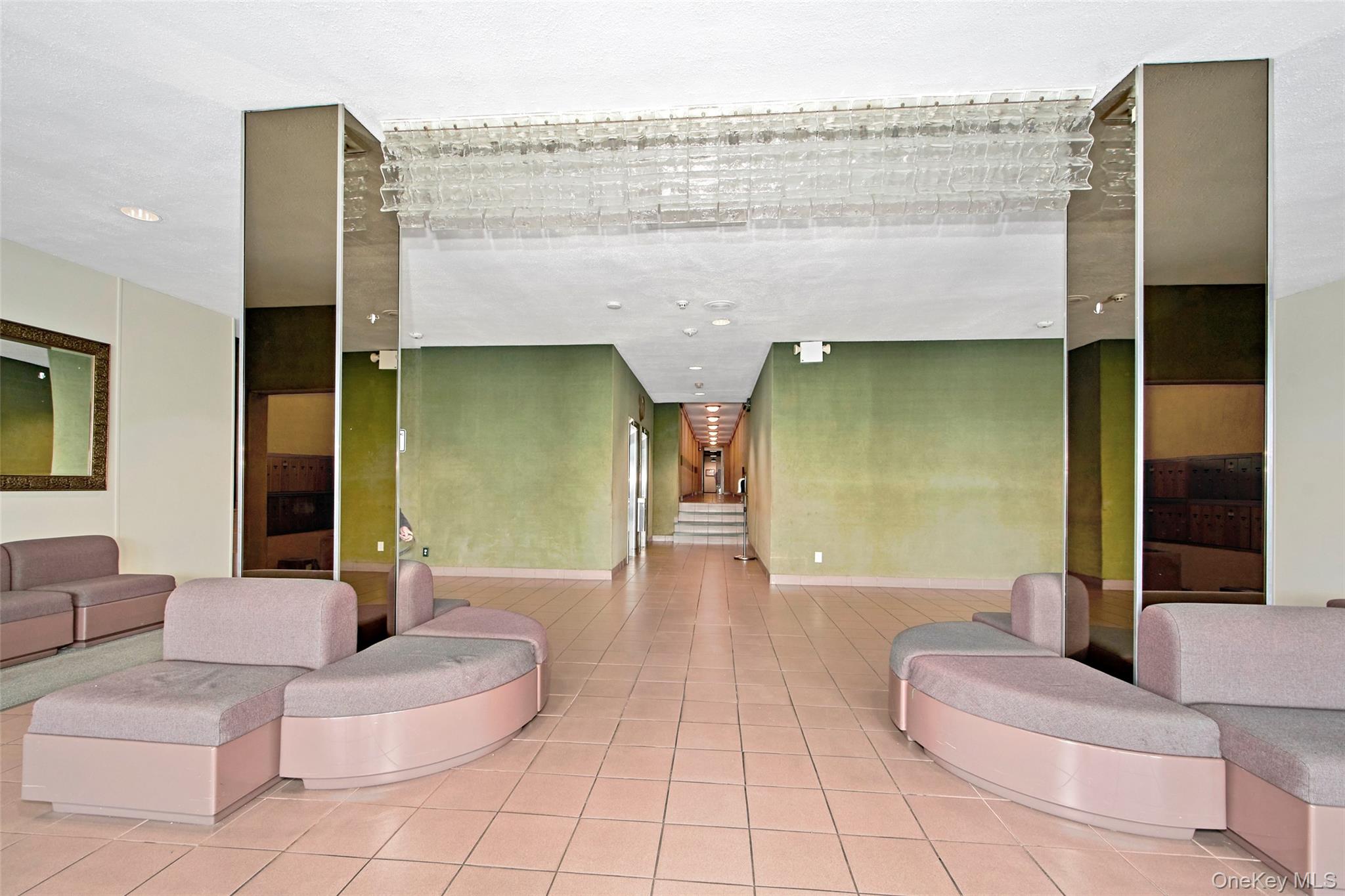 Apartment lobby with curved seating, mirrored columns, and a tiled floor.