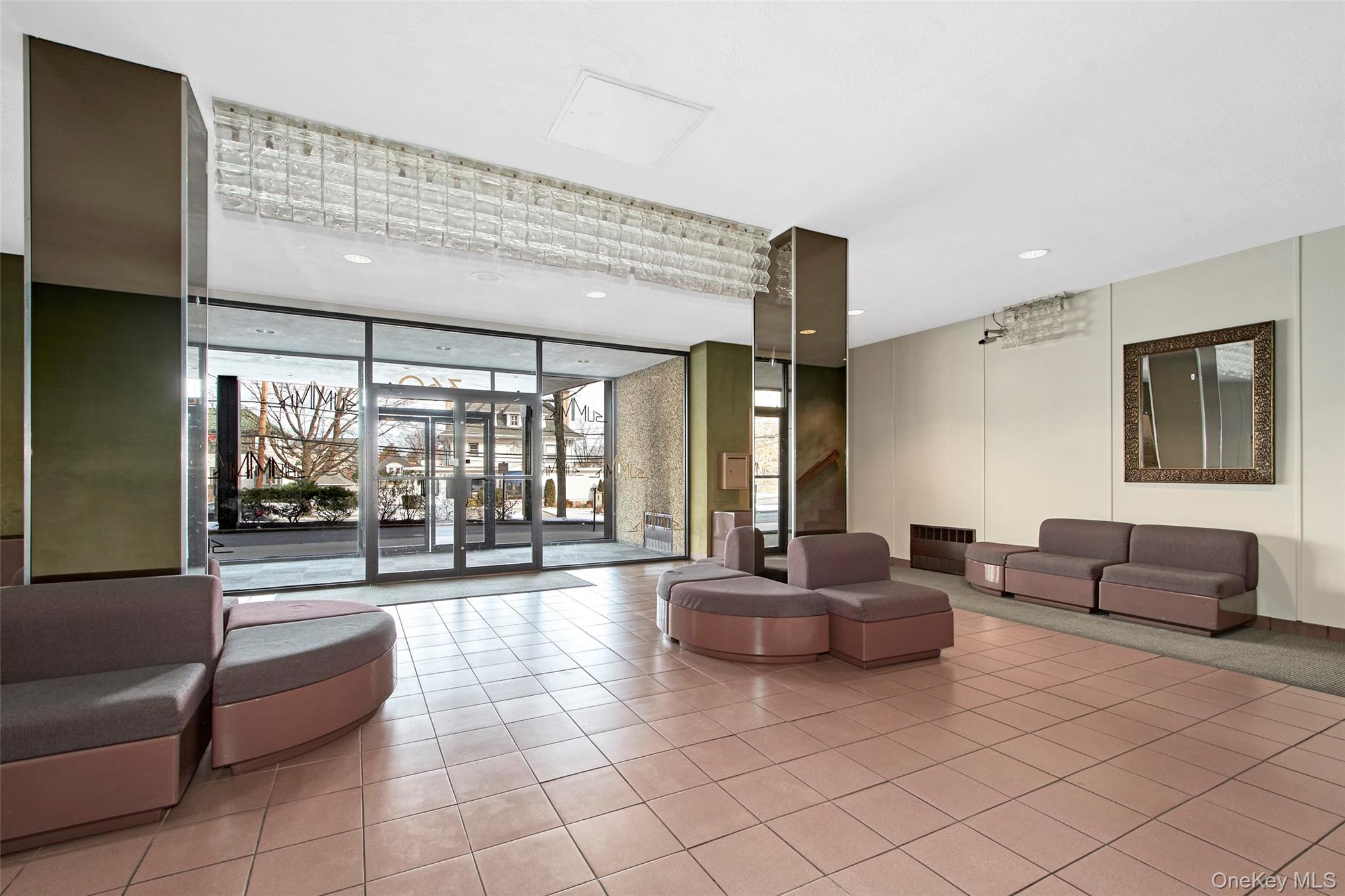 Furnished building lobby with mauve sofas, tiled floors, and glass entrance doors.