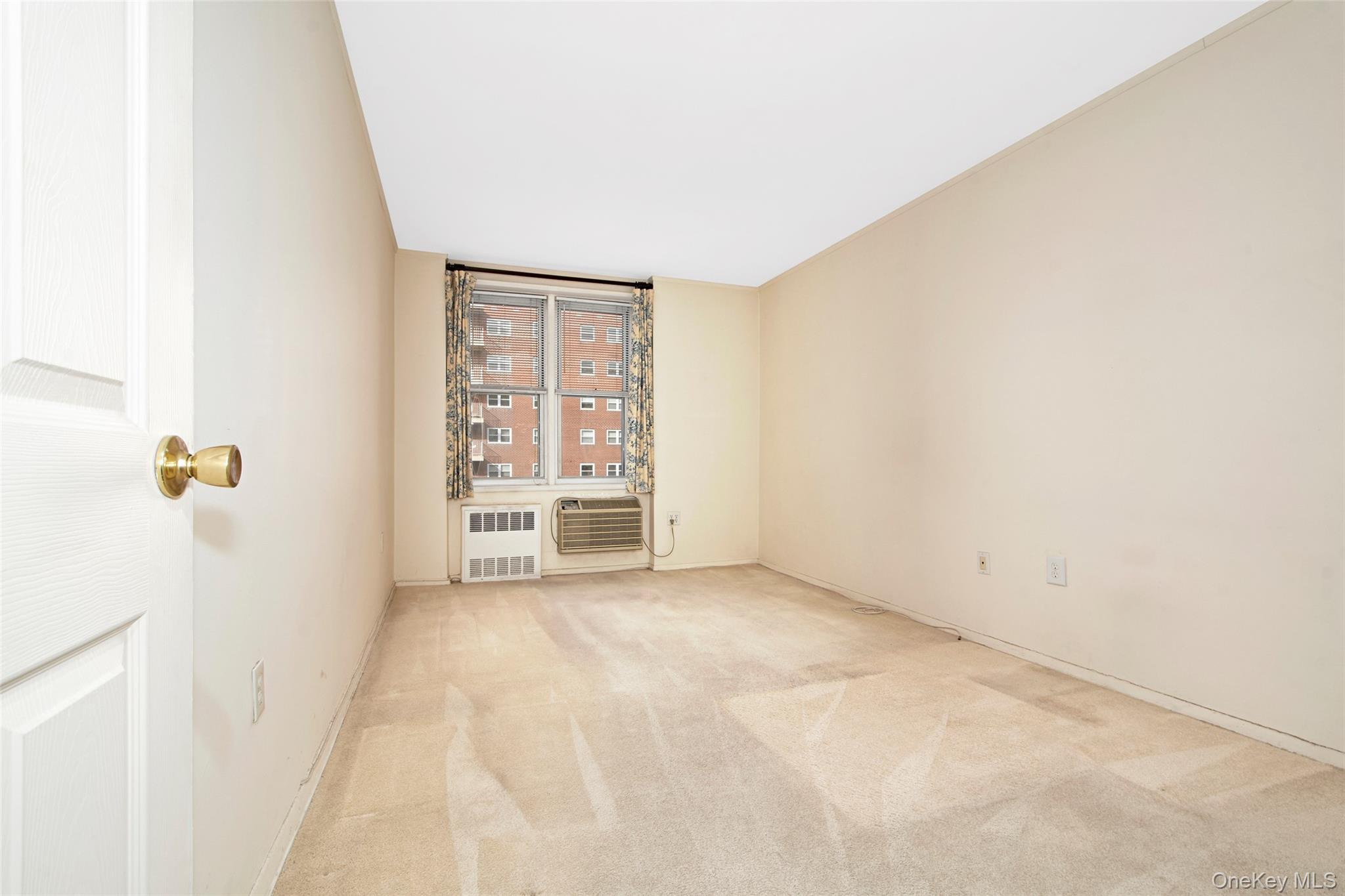 Empty carpeted room with a window, patterned curtains, and a window air conditioner.
