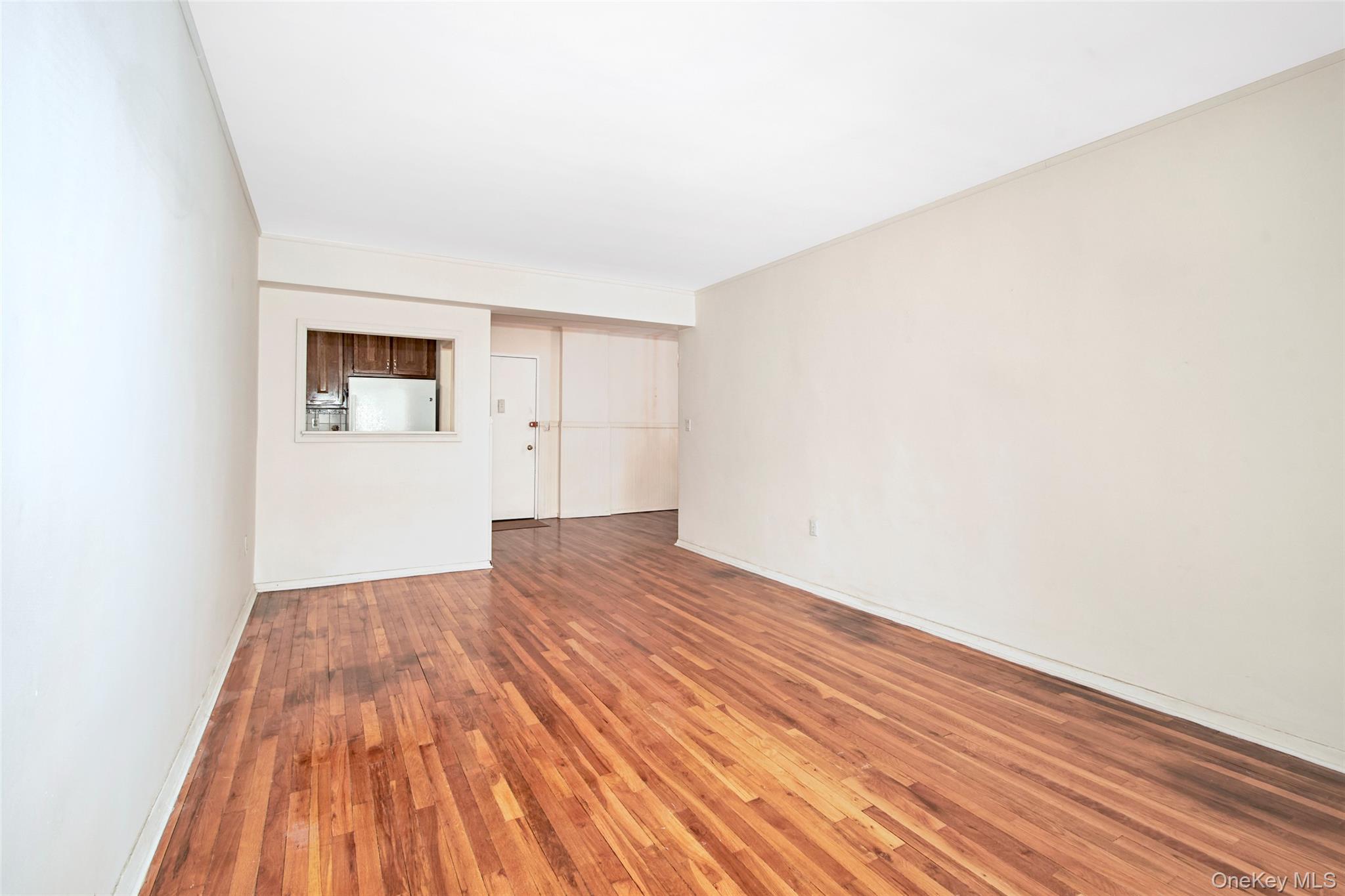 Vacant living room with polished hardwood floors and a pass-through to the kitchen.