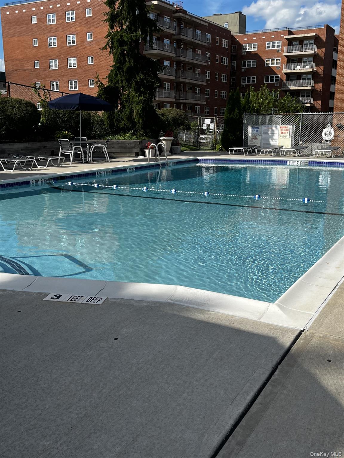 Outdoor swimming pool with a lane rope, lounge chairs, and brick apartment buildings.
