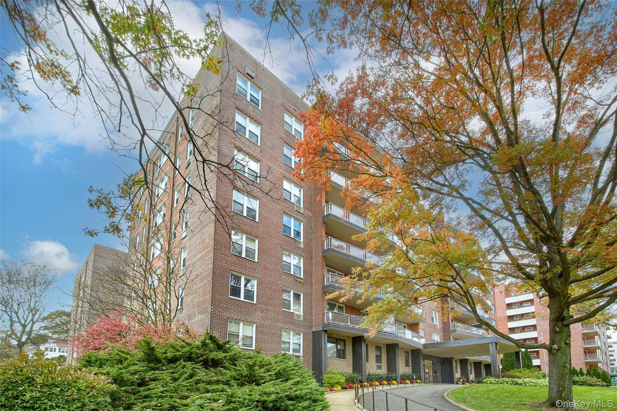 Brick apartment building with balconies and landscaped grounds beneath autumn trees.