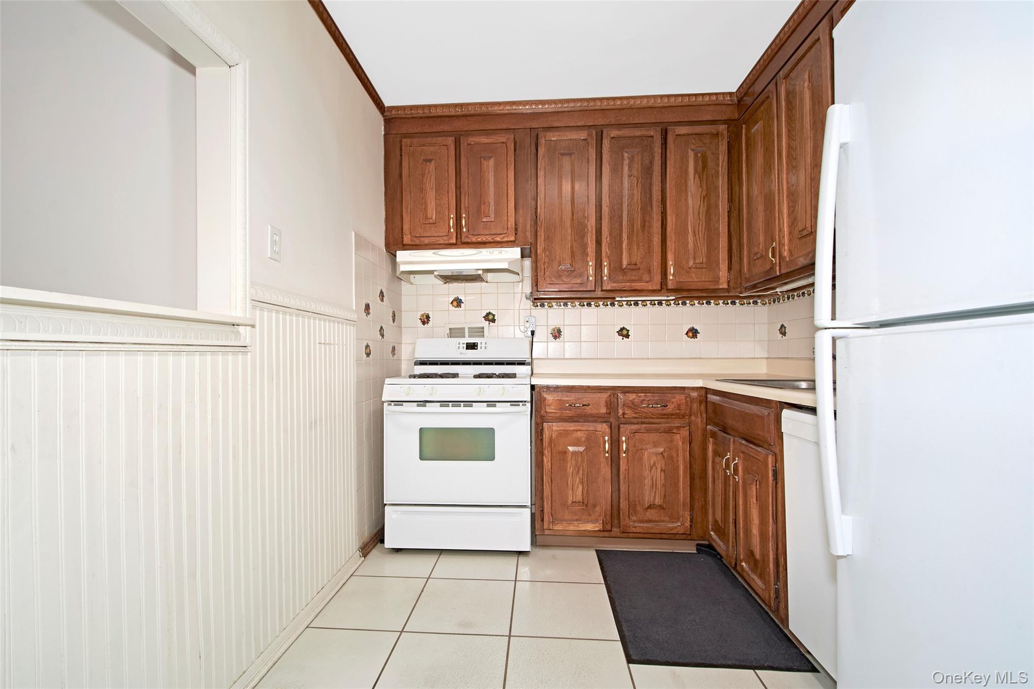 Kitchen with dark wood cabinets, white stove and refrigerator, and tiled backsplash.