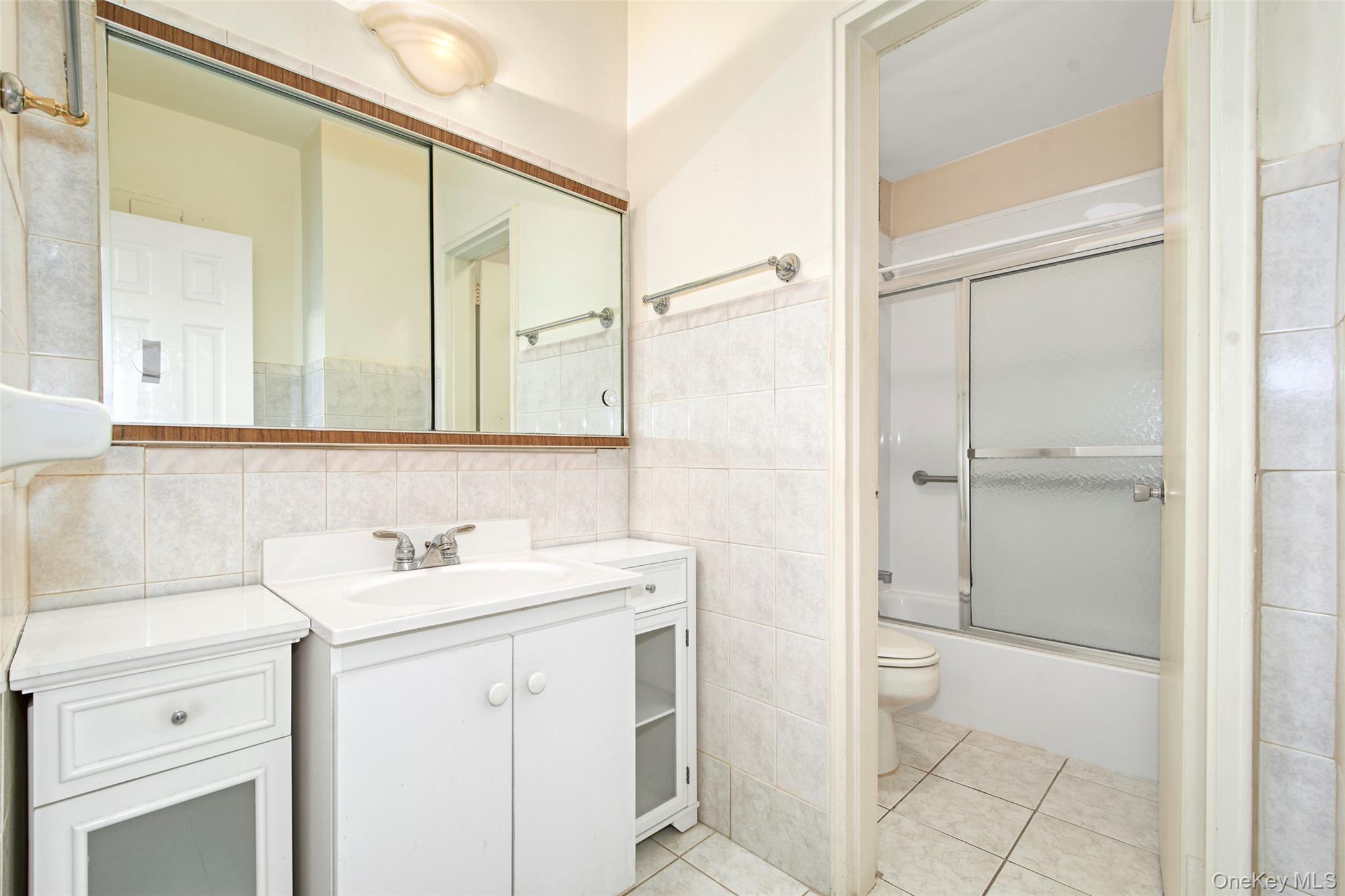 Bathroom with a white vanity, large mirror, and tub with sliding glass shower doors.