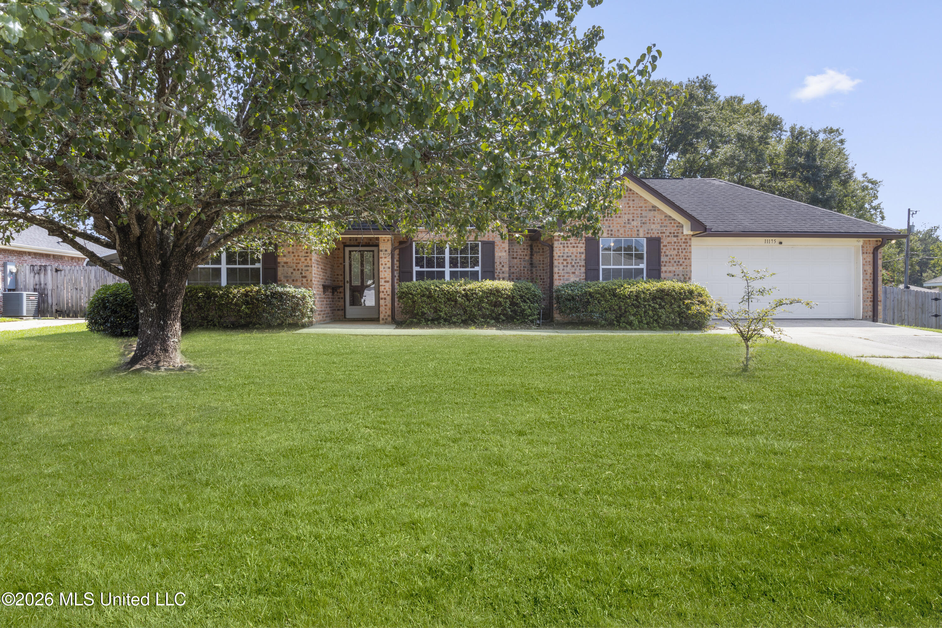 Brick house with attached garage, broad lawn, and a large shade tree in the front yard.