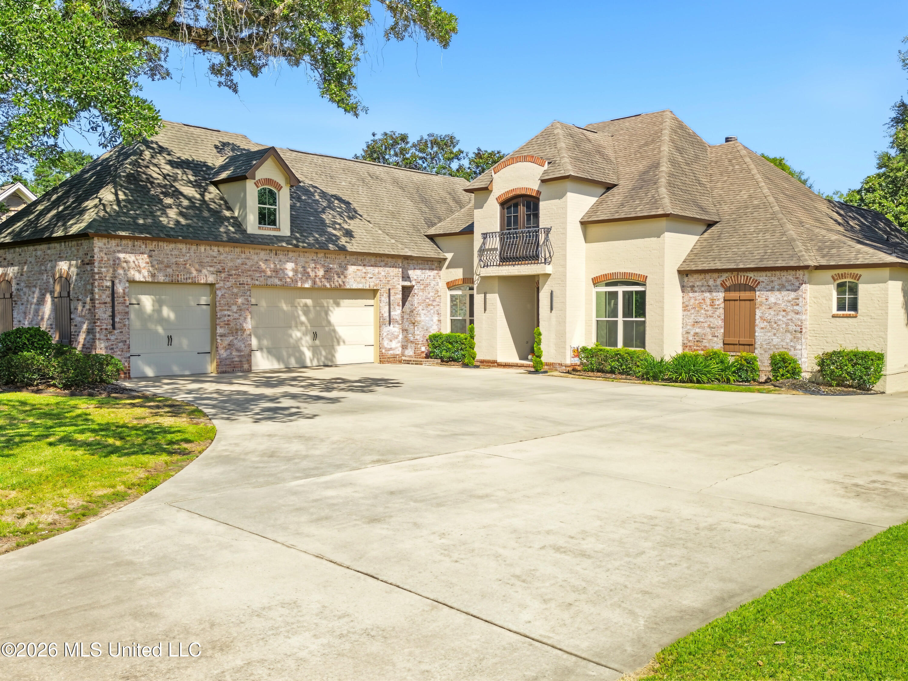 Large brick-and-stucco home with multiple garages, a small balcony, and a broad concrete driveway.