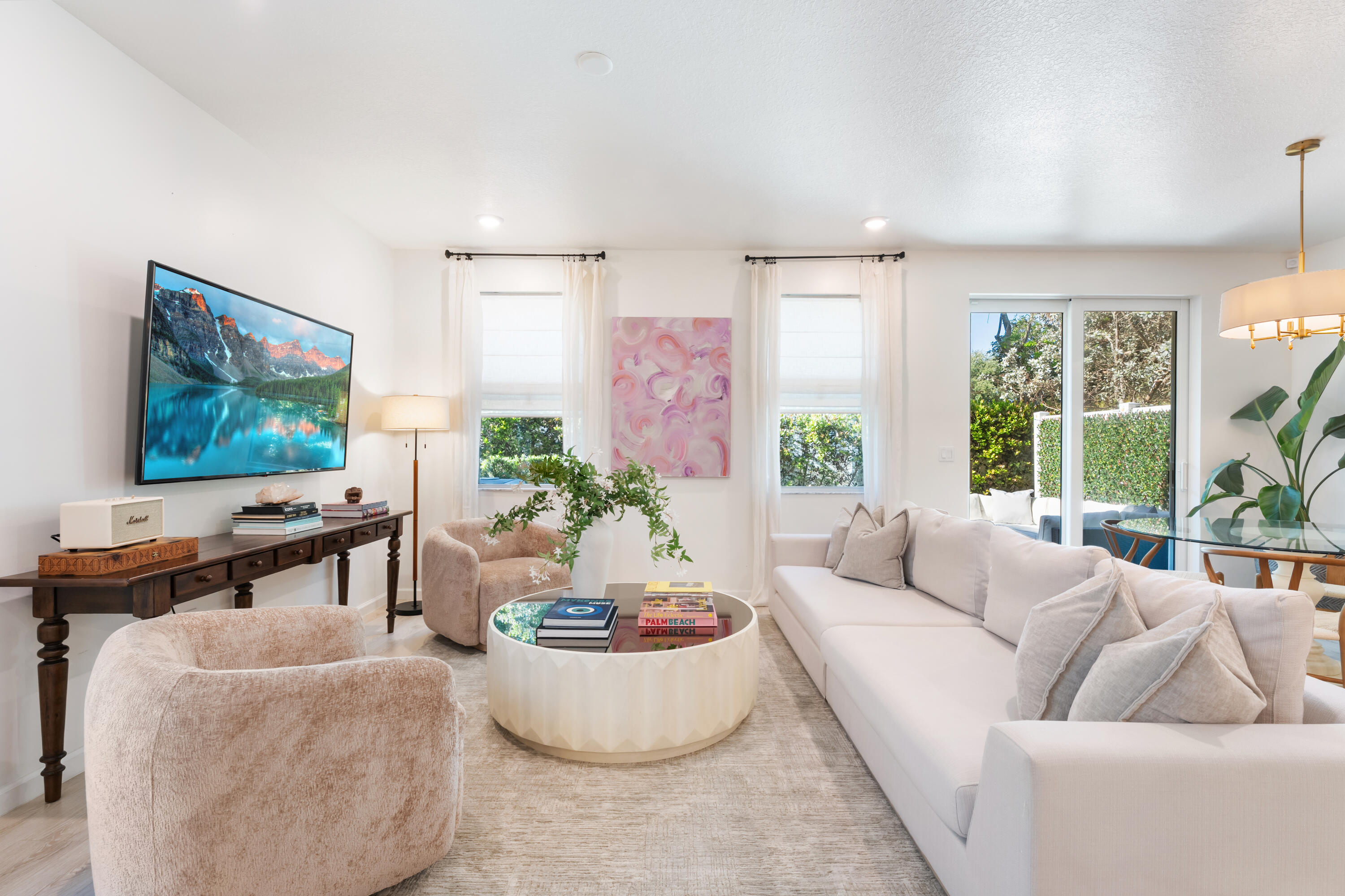 Bright living room with a white sofa, blush chairs, round coffee table, and sliding doors to a garden.