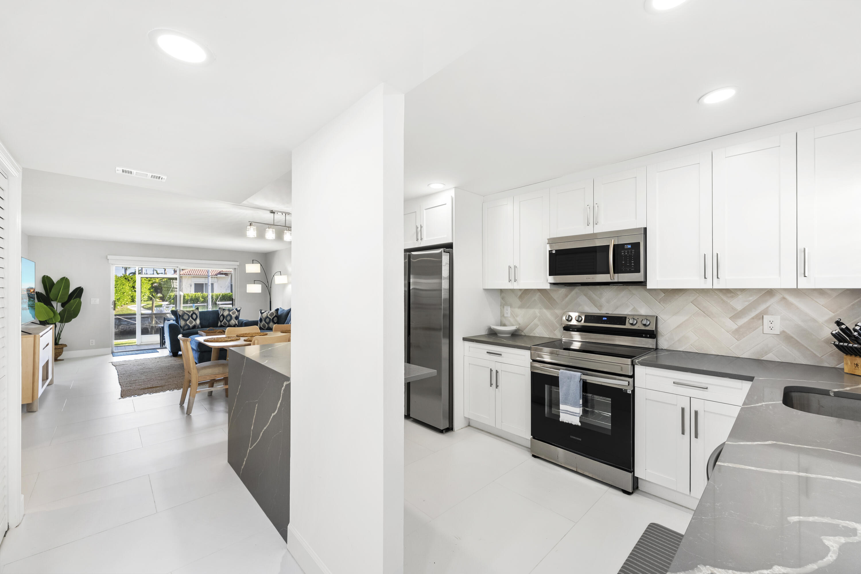 Bright white kitchen with stainless steel appliances, gray counters, and an adjoining living area.