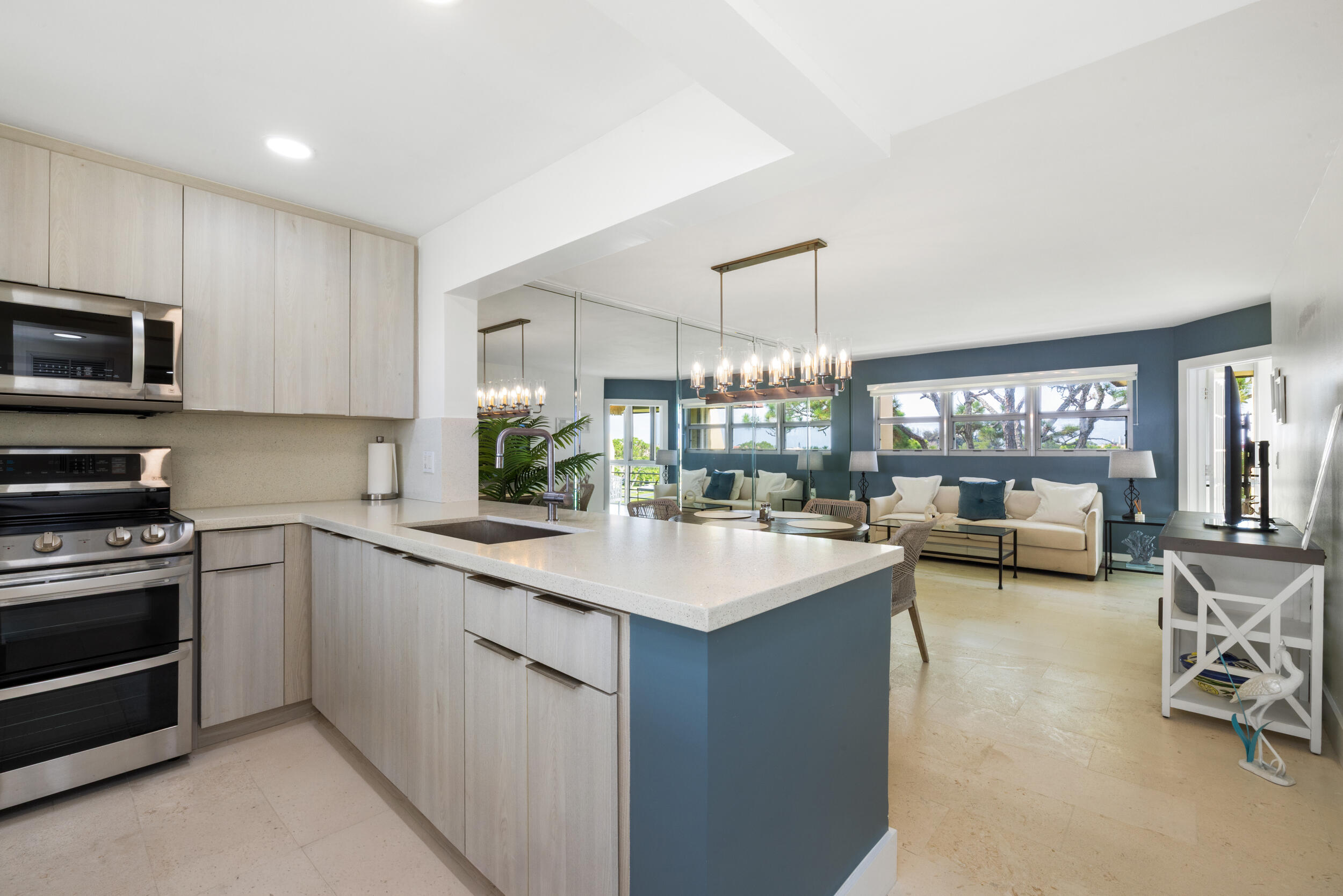 Open-plan kitchen and living room with a large white island, pale wood cabinets, and blue walls.