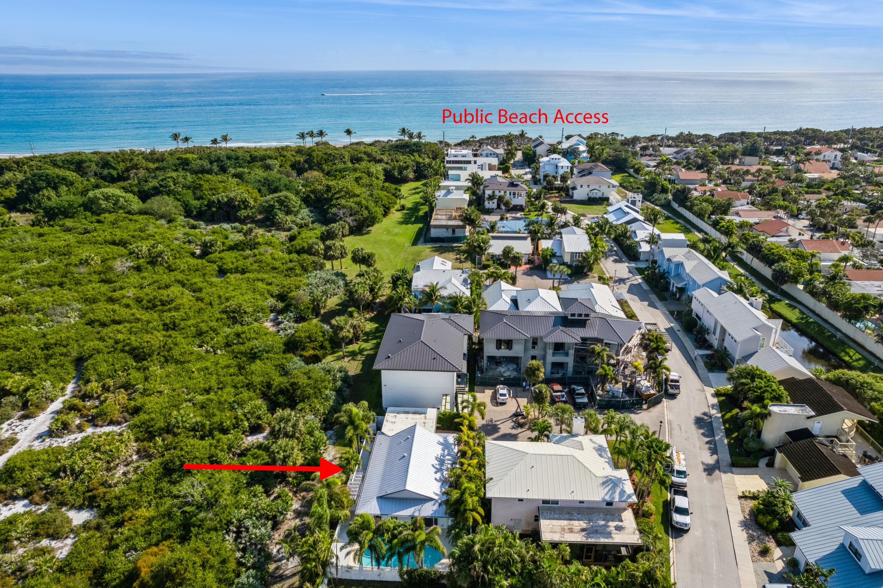 Aerial coastal neighborhood with a red arrow pointing to a light-roofed home beside a green preserve.