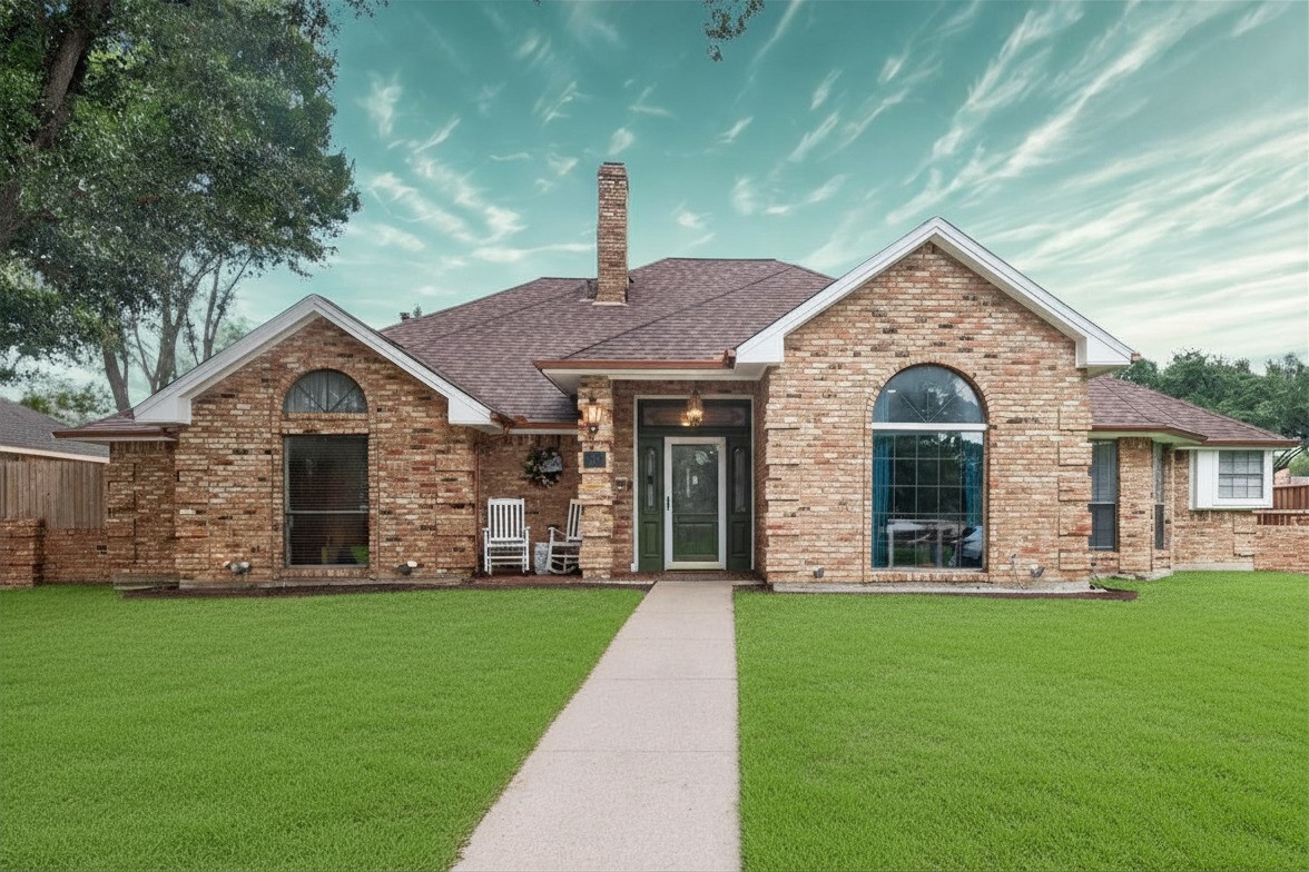 Brick house with arched windows, a green lawn, and a straight walkway to the front door.