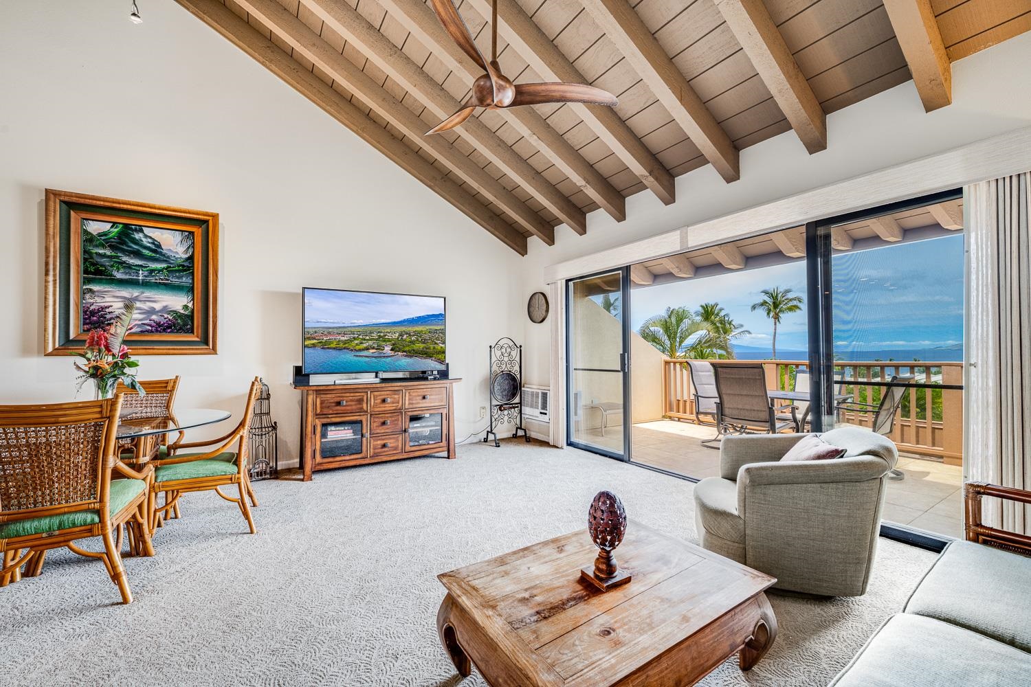 Living room with vaulted wood-beam ceiling and sliding doors opening to an ocean-view balcony.