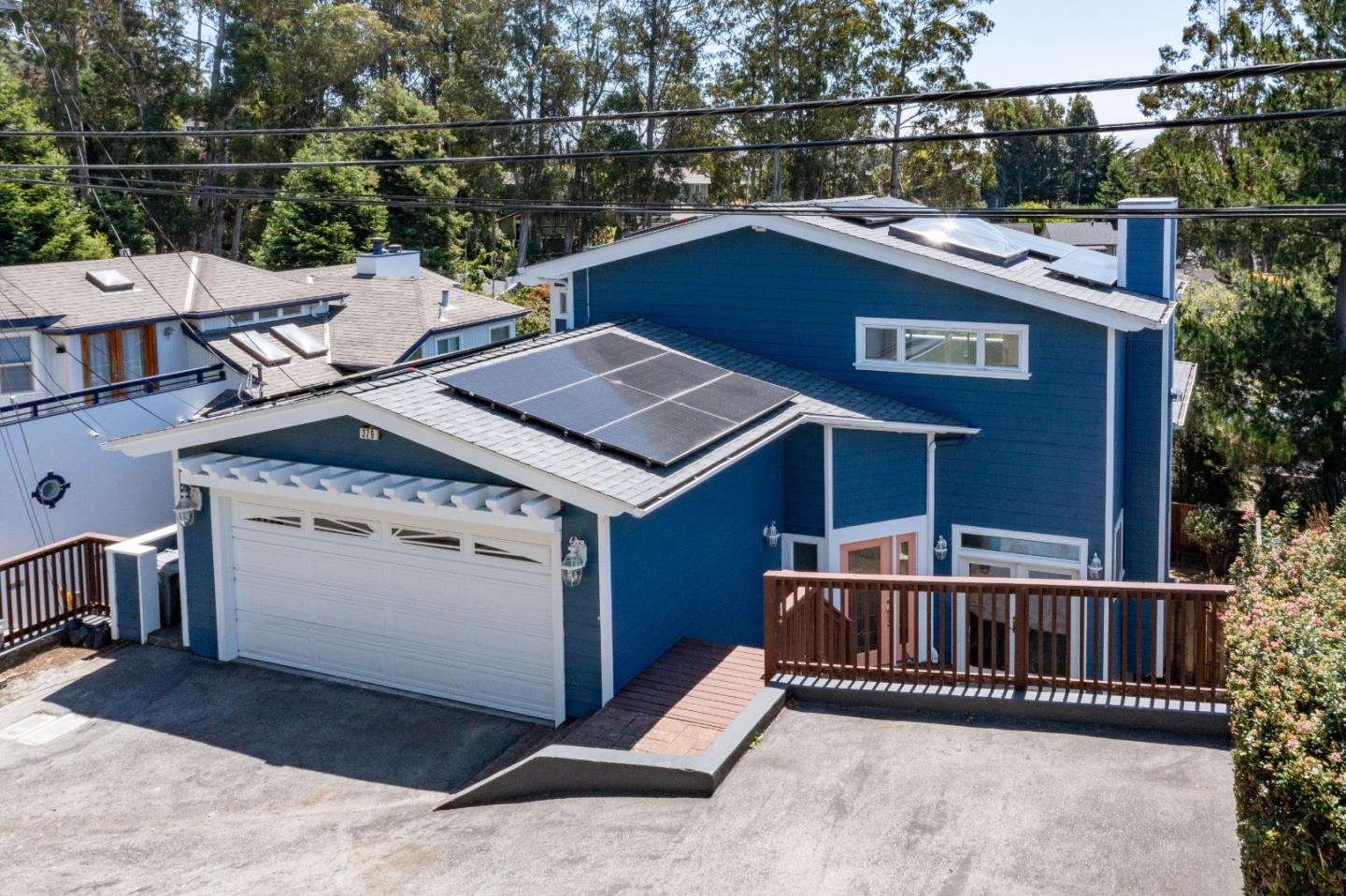 Blue two-story house with rooftop solar panels, a white garage door, and a paved driveway.