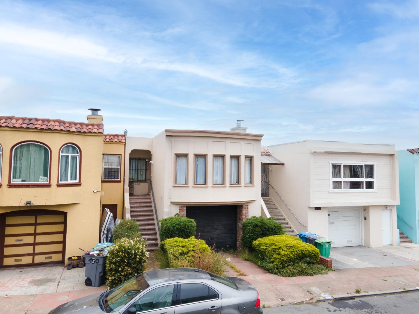 Row of homes with varied facades, front steps, shrubs, and a parked car.
