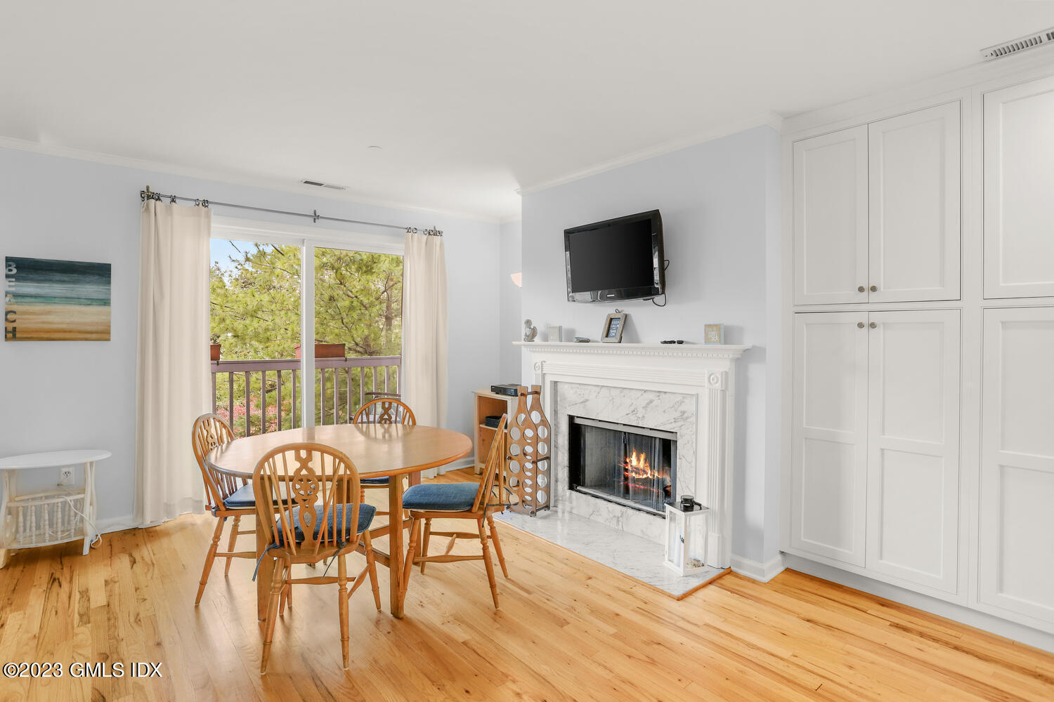 Dining and living area with a marble fireplace, hardwood floors, built-in cabinets, and balcony doors.