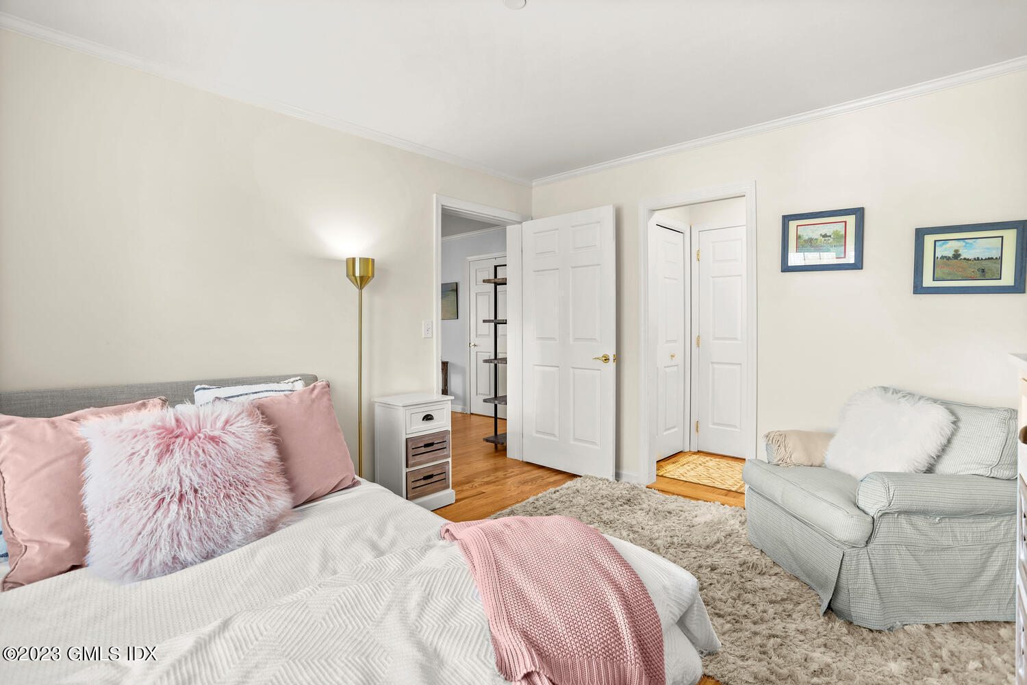 Staged bedroom with pink accents, a gray armchair, shag rug and hardwood floors.
