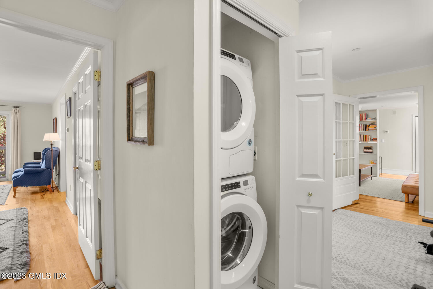 Hallway laundry closet with stacked washer and dryer, opening onto bright furnished rooms.
