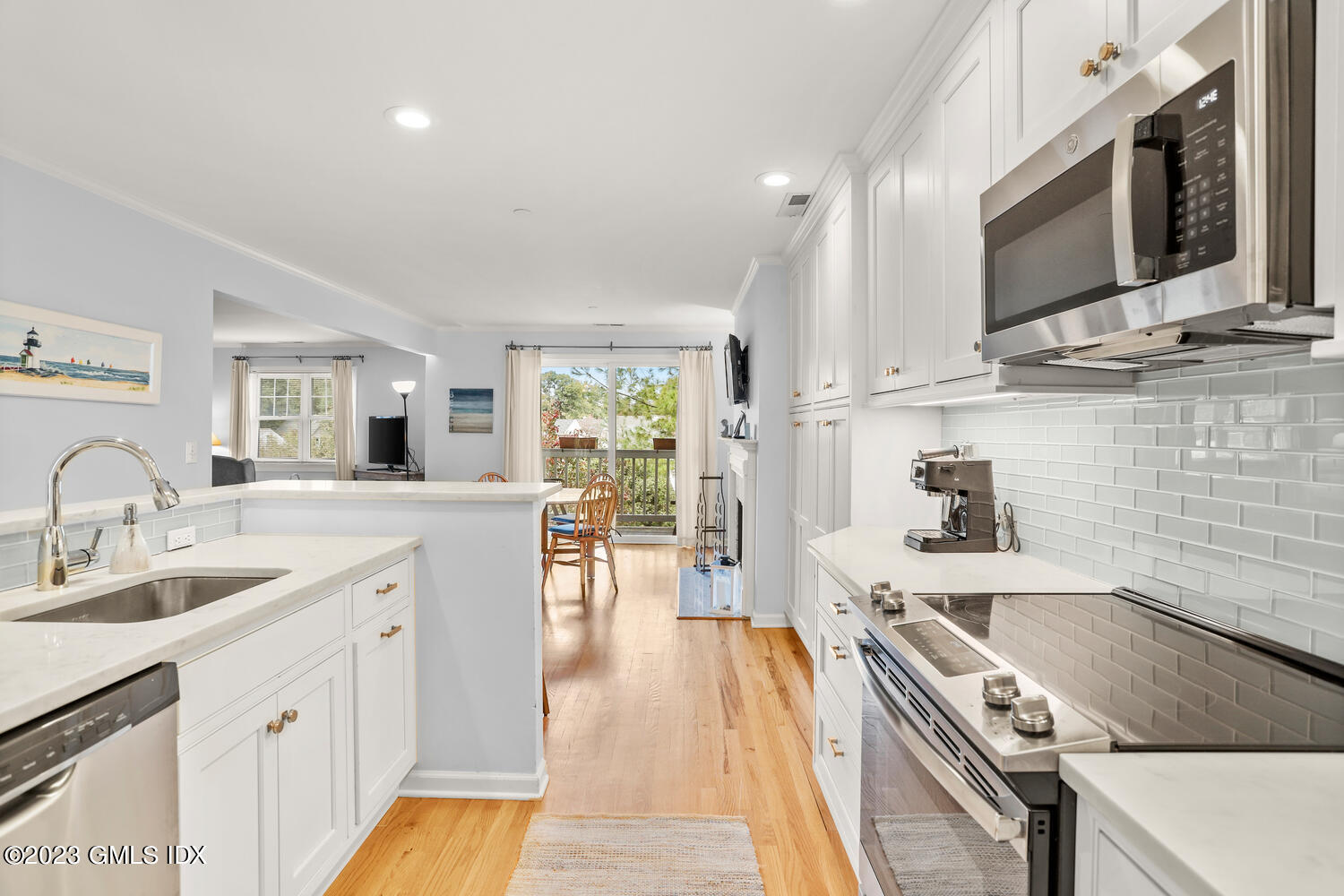 Apartment kitchen with white cabinets, stainless steel appliances, and an open dining area by balcony doors.