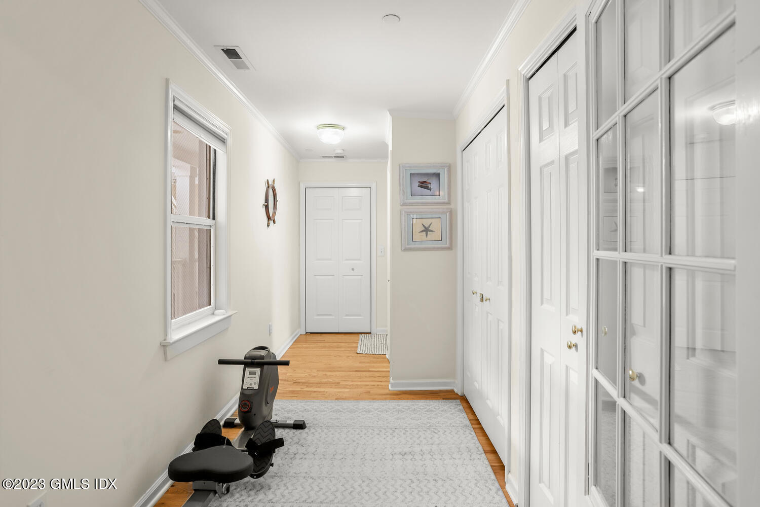 Apartment hallway with white paneled doors, hardwood flooring, and an exercise bike beside a patterned rug.