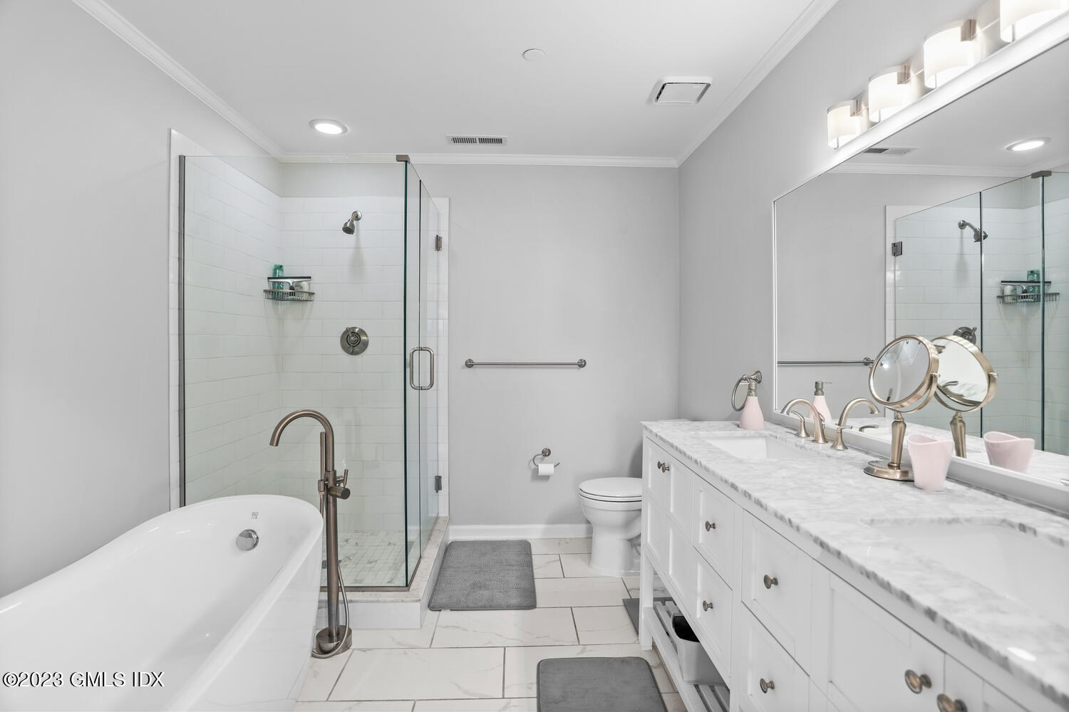 Bathroom with a freestanding tub, glass shower, and long white double vanity.