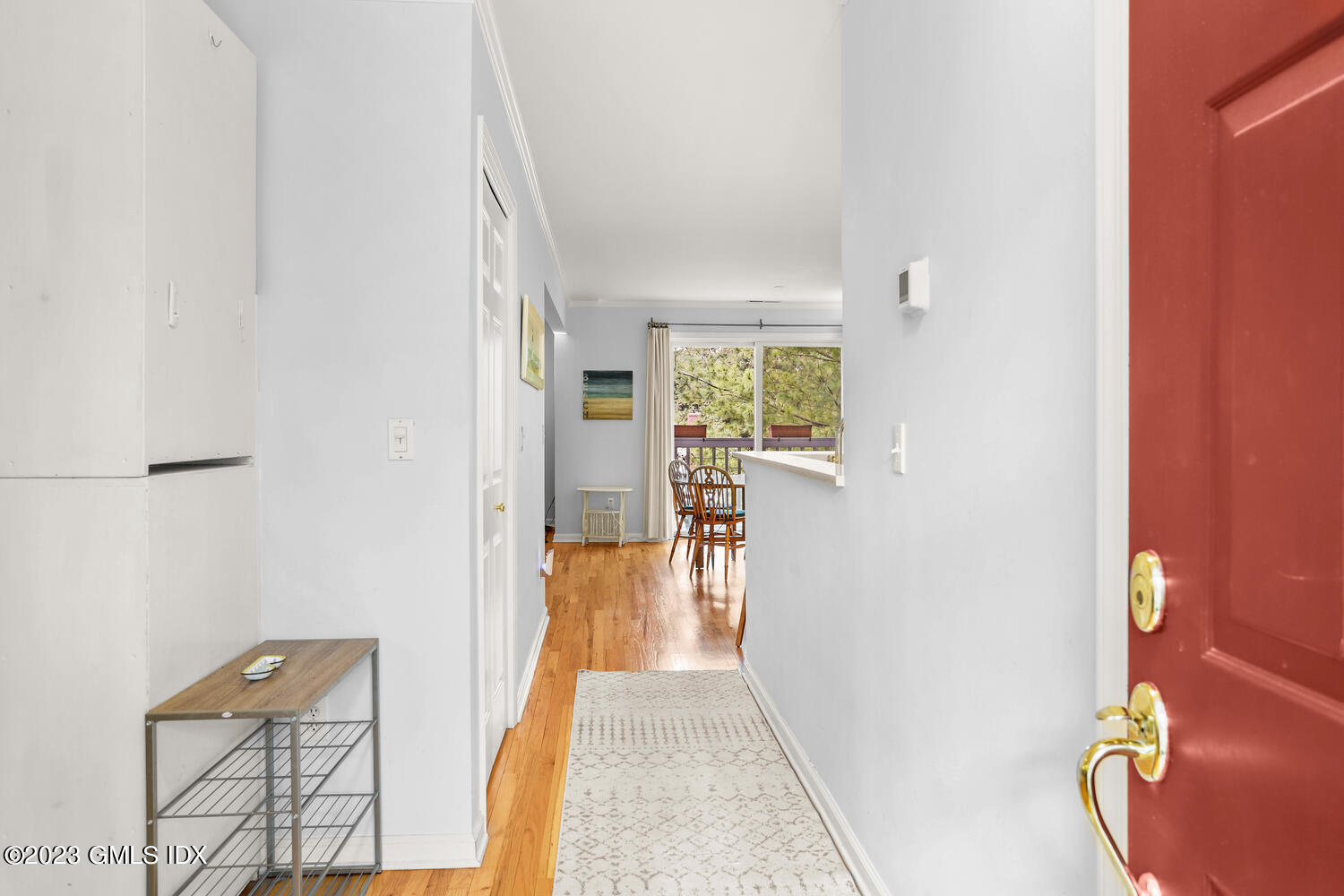 Apartment entry hallway with a red front door, hardwood floors, and dining area by a large window.
