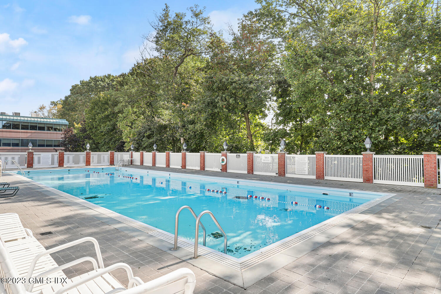 Outdoor swimming pool with lap lanes, brick-and-white fencing, and lounge chairs.