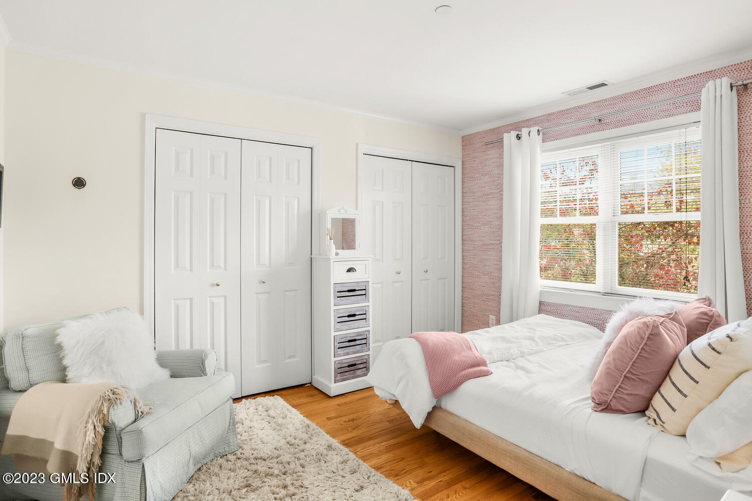 Bright bedroom with a white bed, pink accents, closet doors, and a large window.