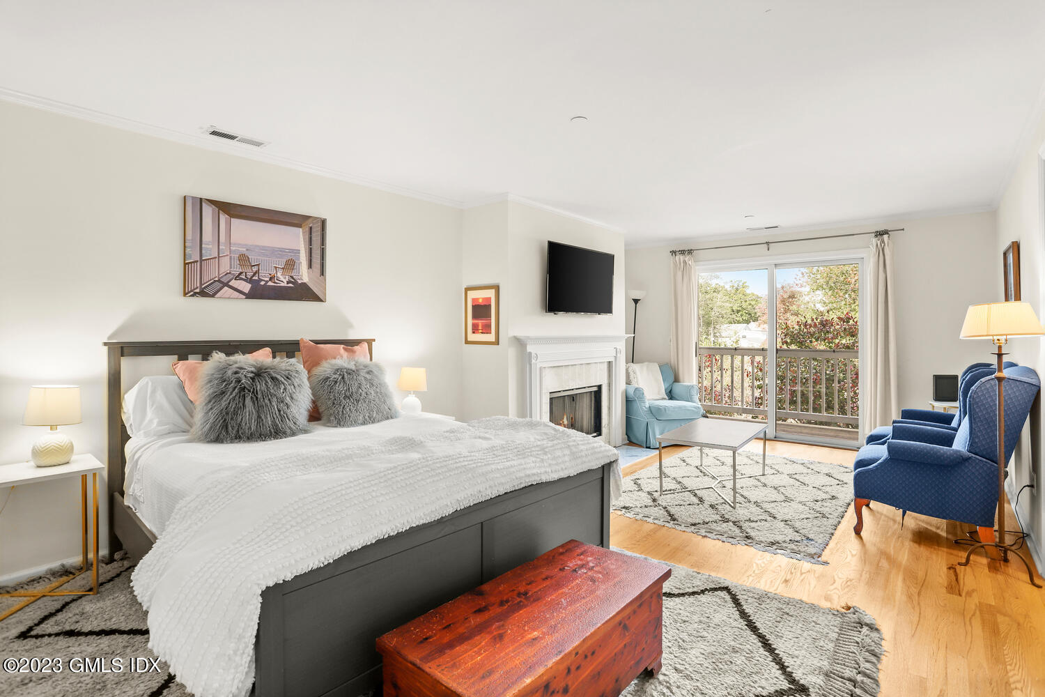 Furnished bedroom with a fireplace, blue sitting chairs, and sliding glass doors to a balcony.